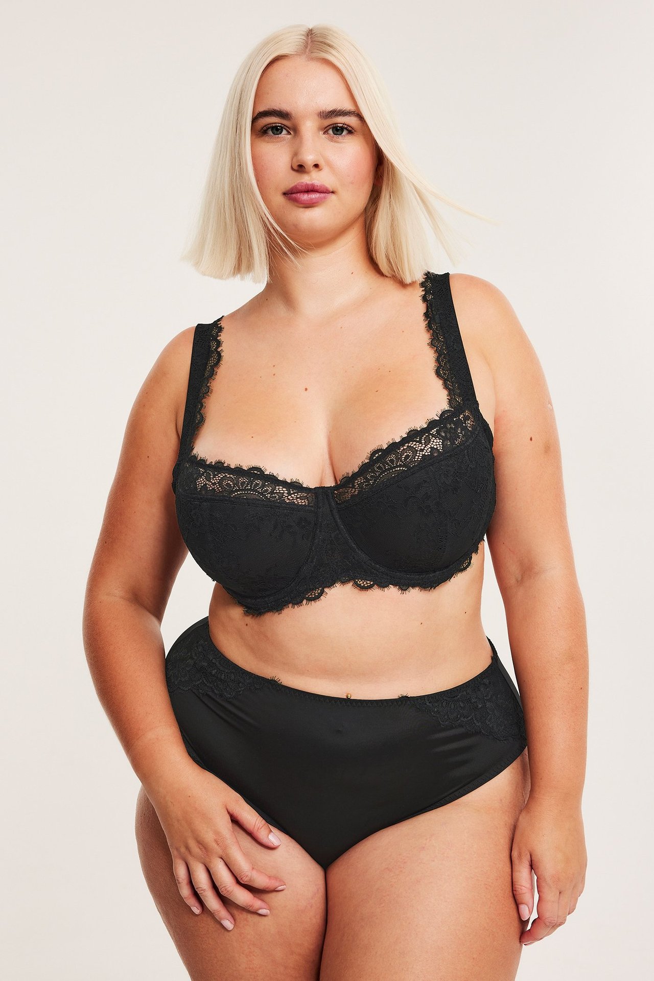 Frontvy av kvinna i svart spetsbalconette-bh med lätt vaddering och matchande svarta spetstrosor.