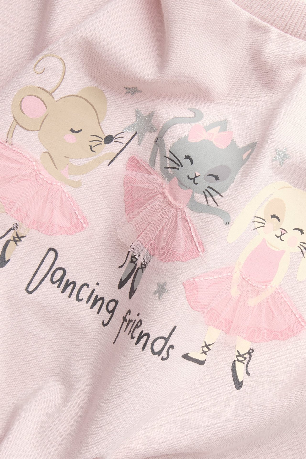 Zbliżenie na jasnoróżową bluzkę dziecięcą z nadrukiem "Dancing friends" i tiulowymi falbankami.