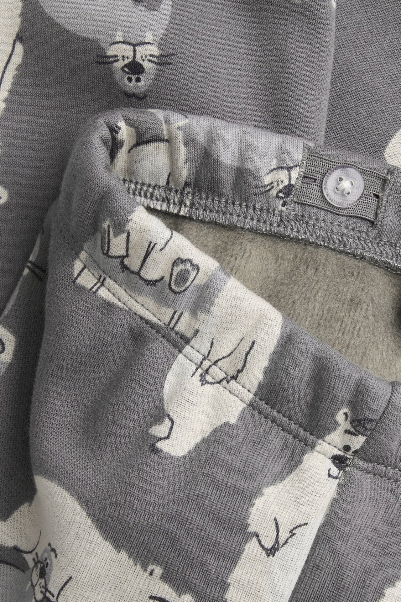 Närbild på barns grå värmande leggings med isbjörnsmönster, justerbar knappmidja och mjukt fleecefoder.