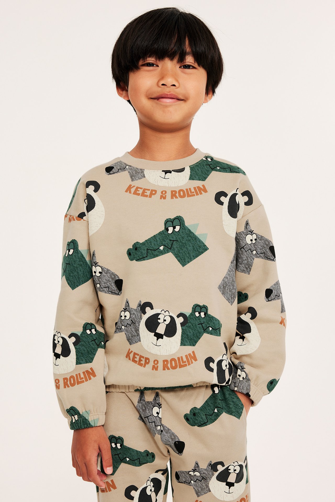 Frontvy av ett barn i en beige bomullssweatshirt med djurmönster och matchande mjukisbyxor.