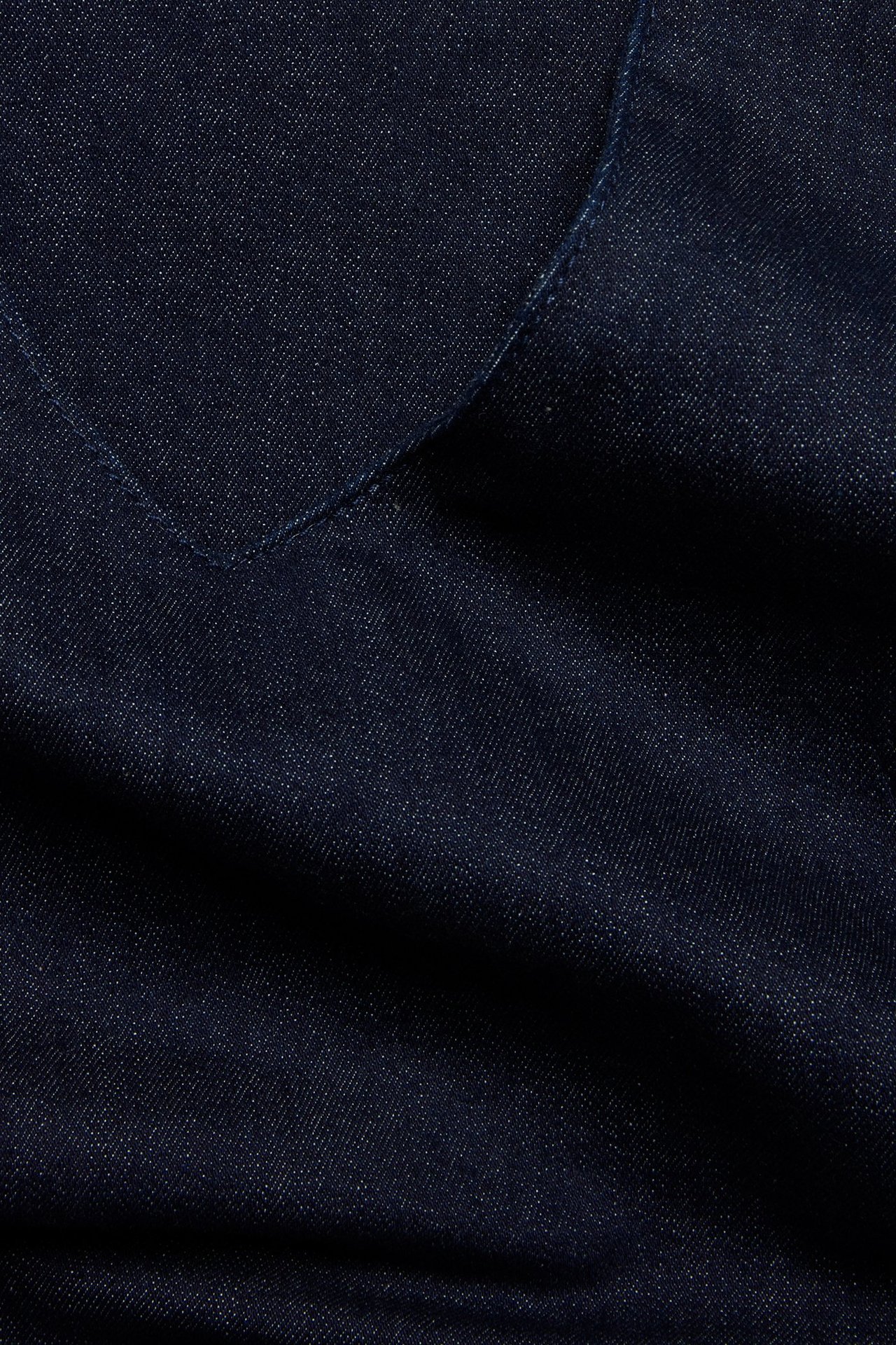 Zbliżenie ciemnego dżinsowego materiału na sukienkę, z widocznymi detalami szwów.