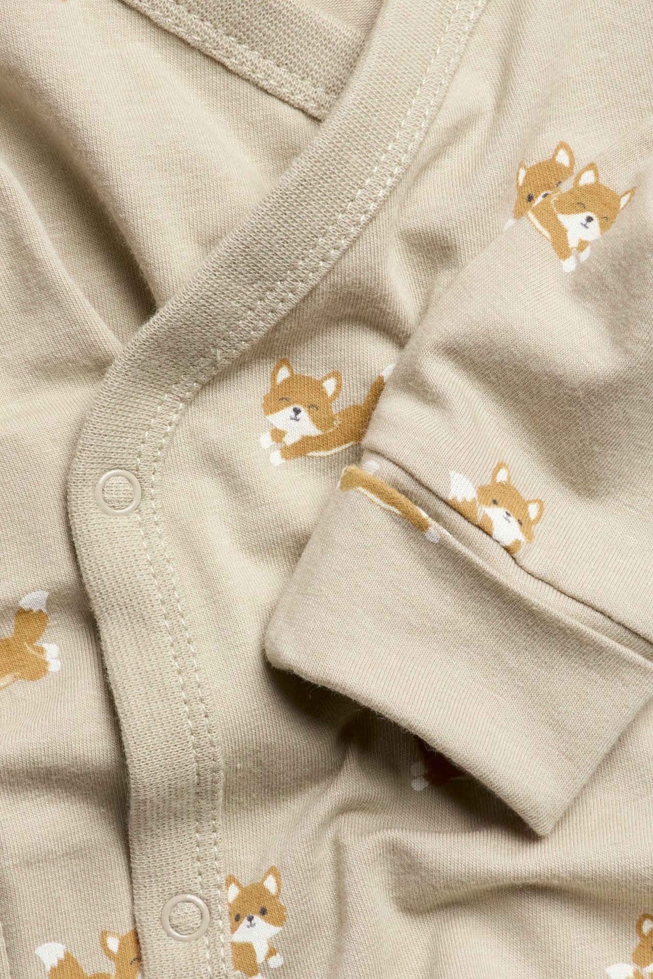Zbliżenie beżowego body niemowlęcego we wzór lisów, z zatrzaskami i wywijanymi mankietami.