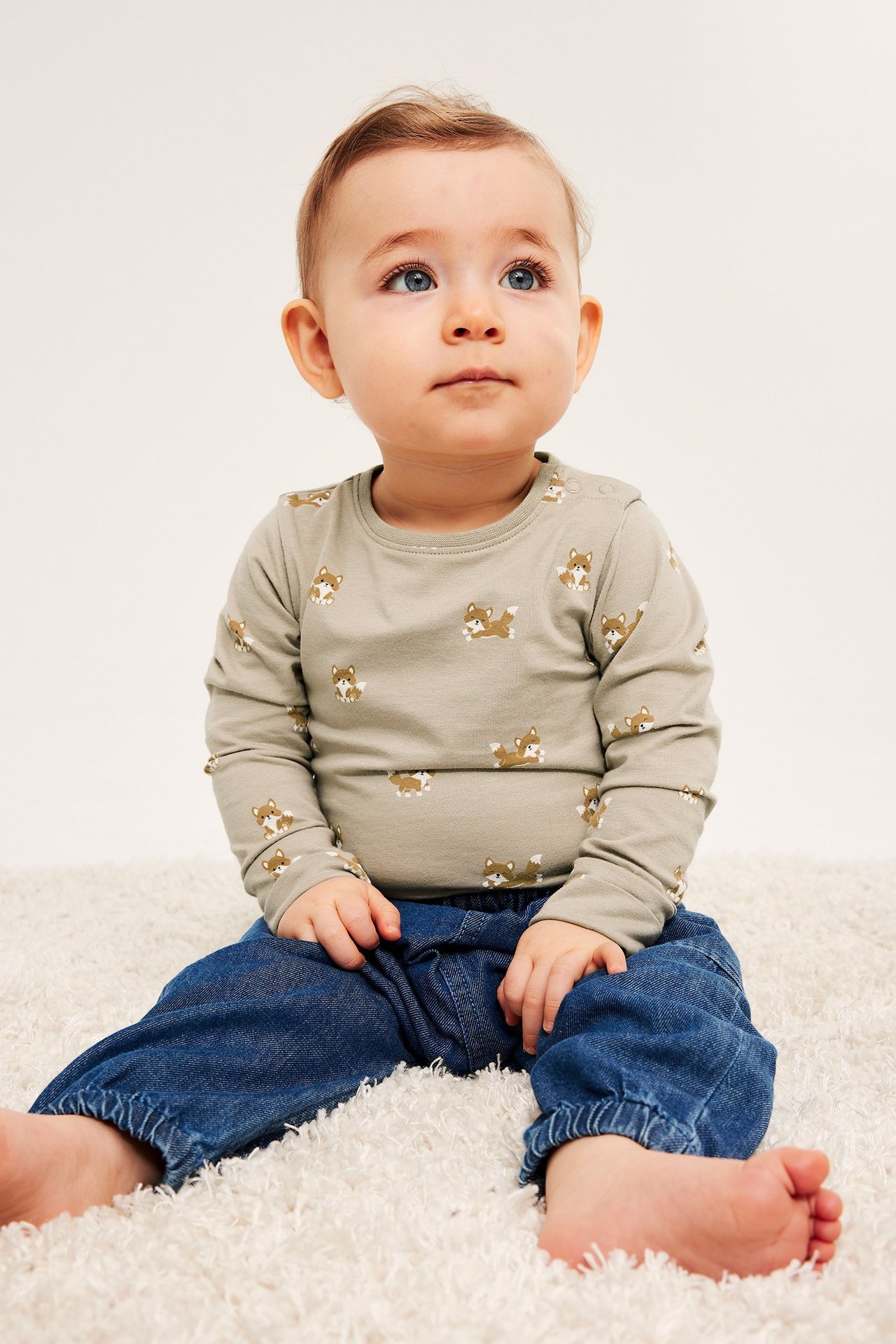 Edestä, vauva yllään beige pitkähihainen body kettukuviolla ja siniset housut.
