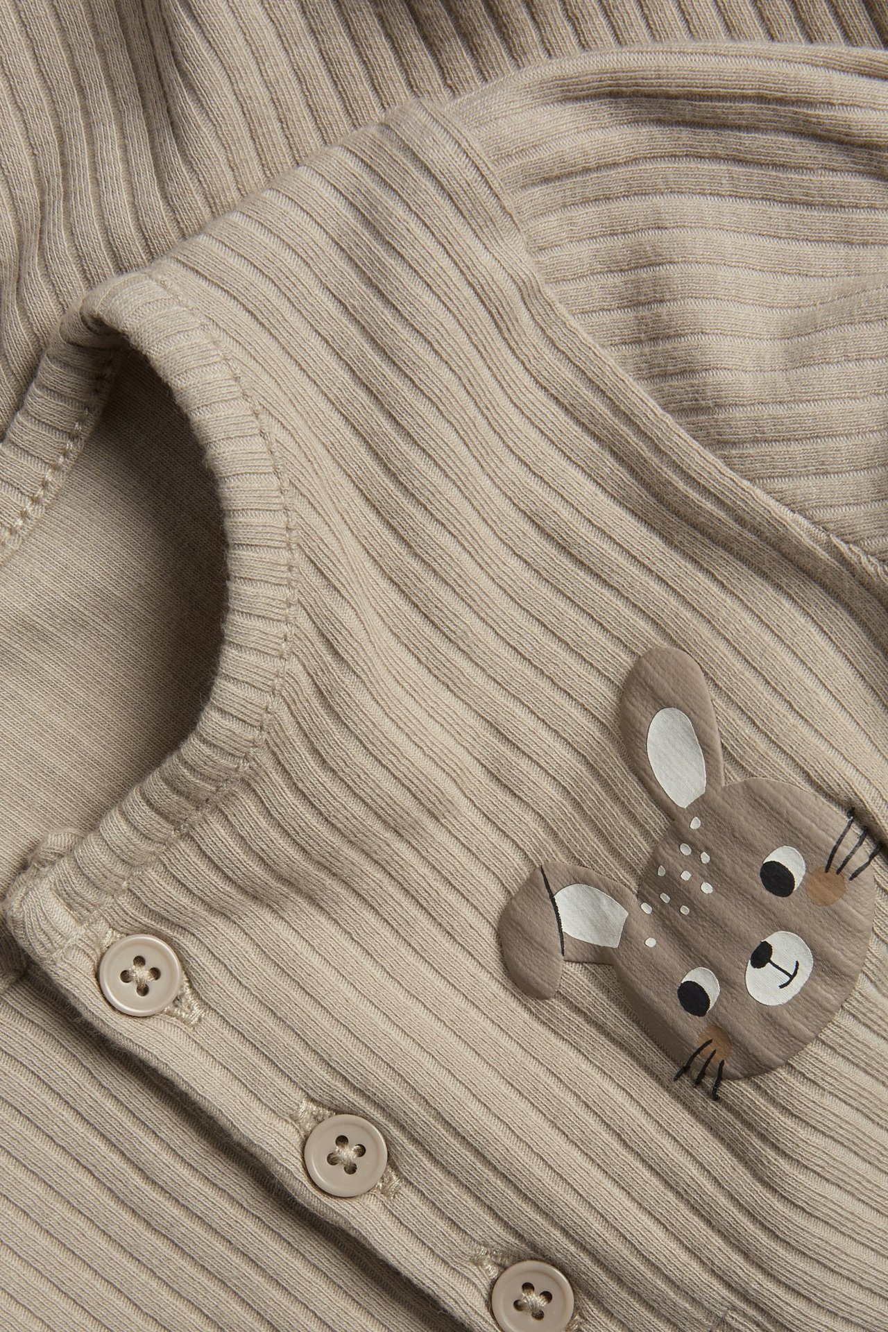 Zbliżenie beżowego prążkowanego body niemowlęcego z guzikami z przodu i brązowym nadrukiem jelenia na piersi.