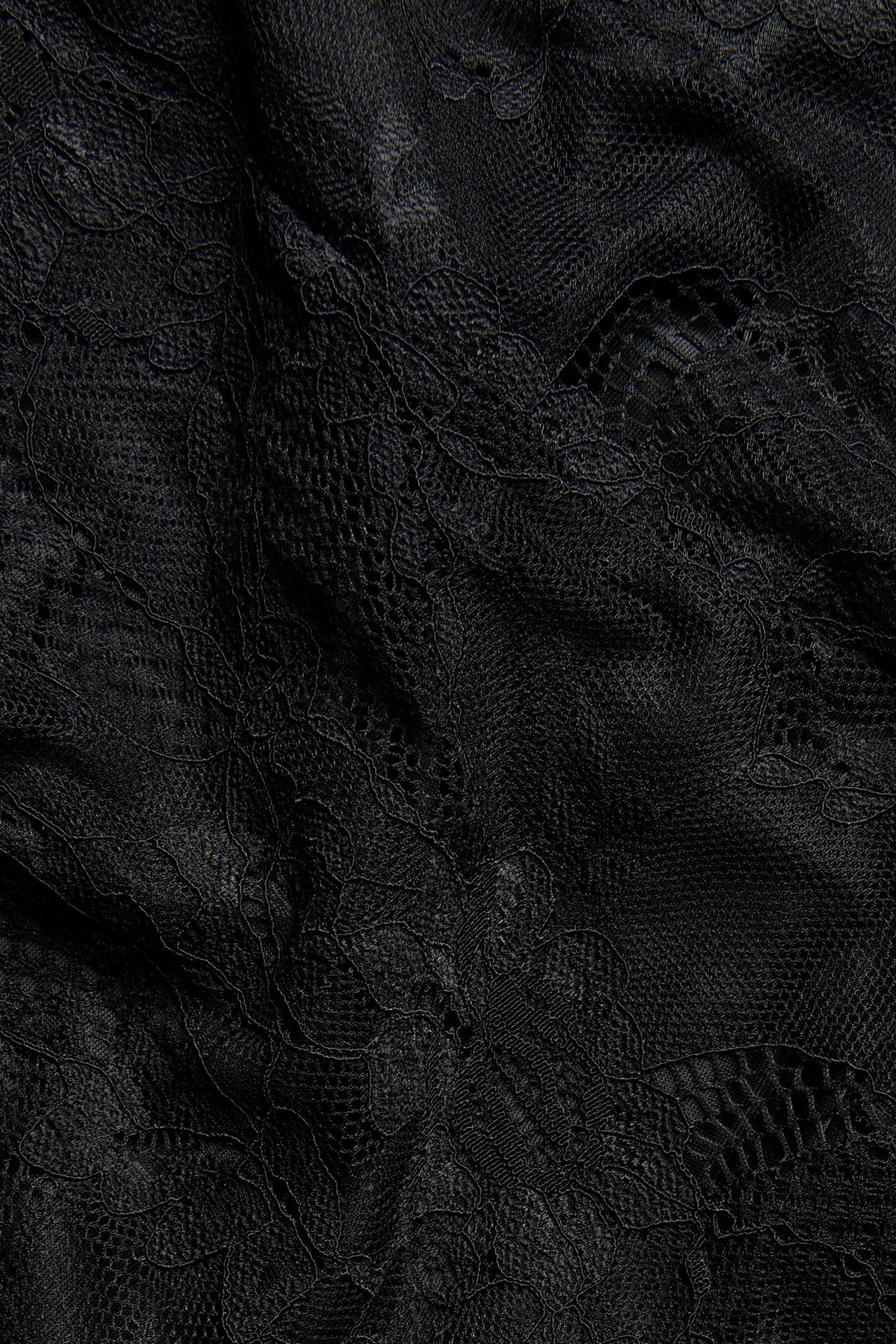 Zbliżenie czarnej koronkowej spódnicy, ukazujące misterny wzór kwiatowy na prześwitującym materiale.