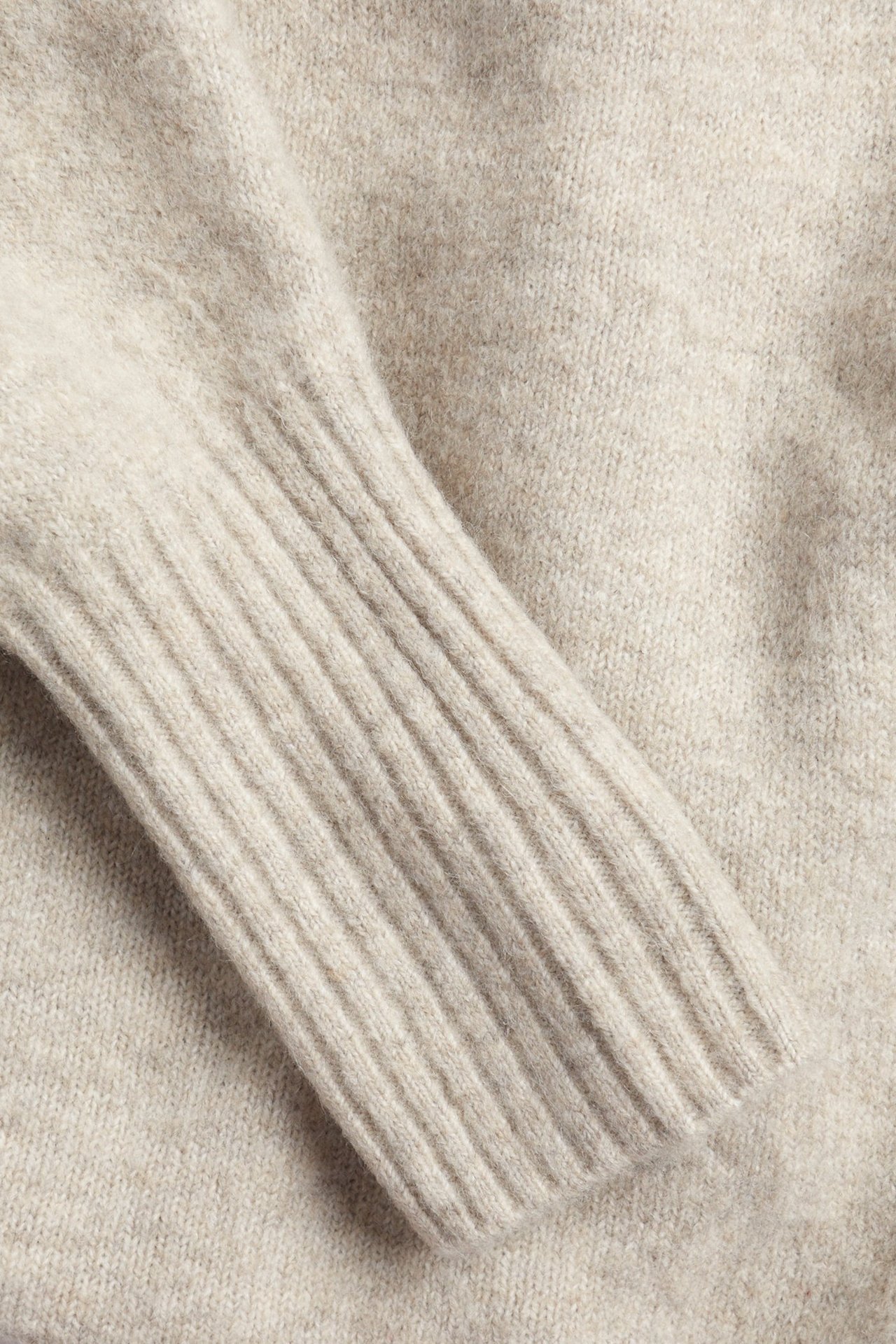 Zbliżenie beżowej dzianinowej długiej sukienki z prążkowanym mankietem.