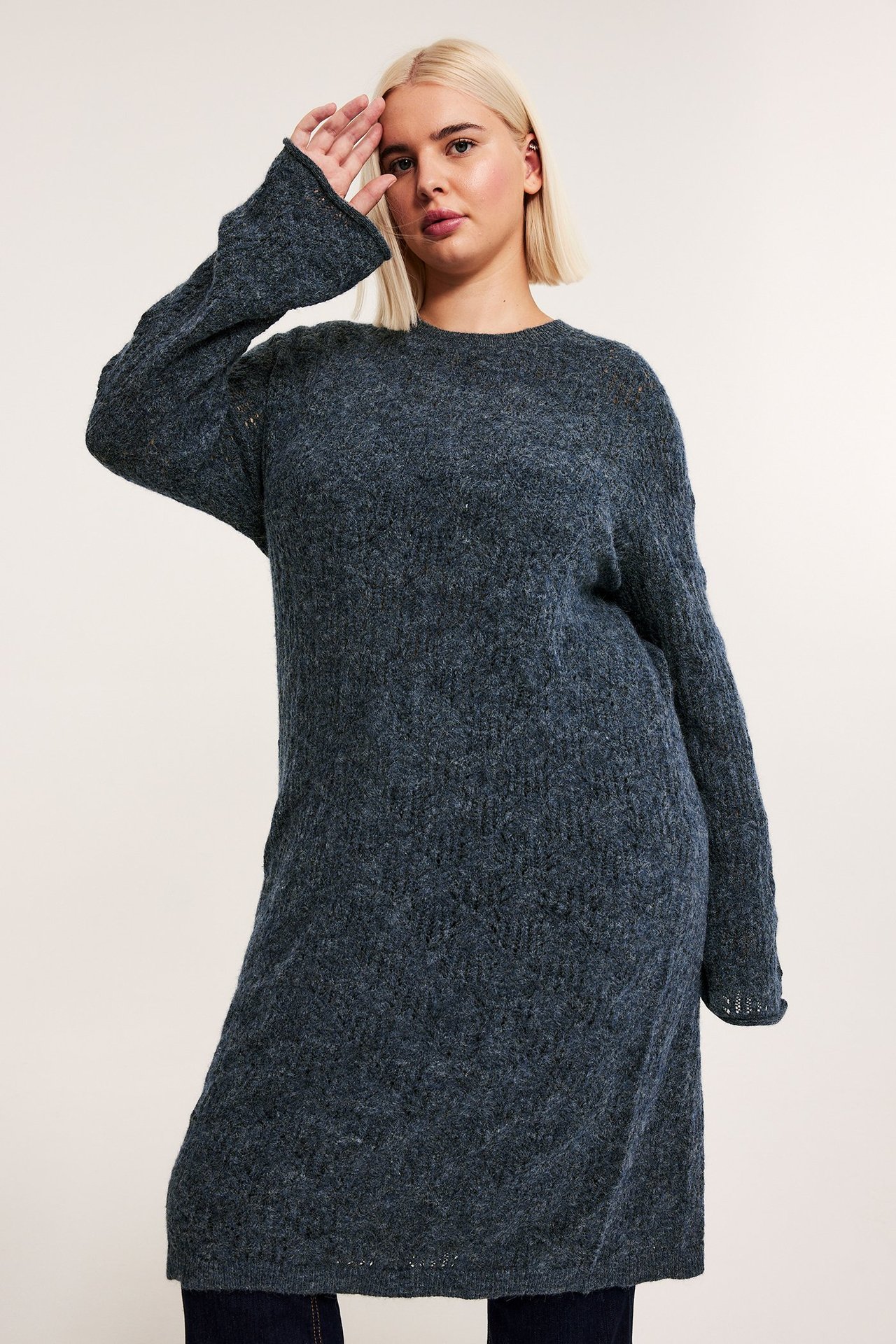 Framifrån, kvinna i mörkblå lösstickad klänning över mörka jeans.