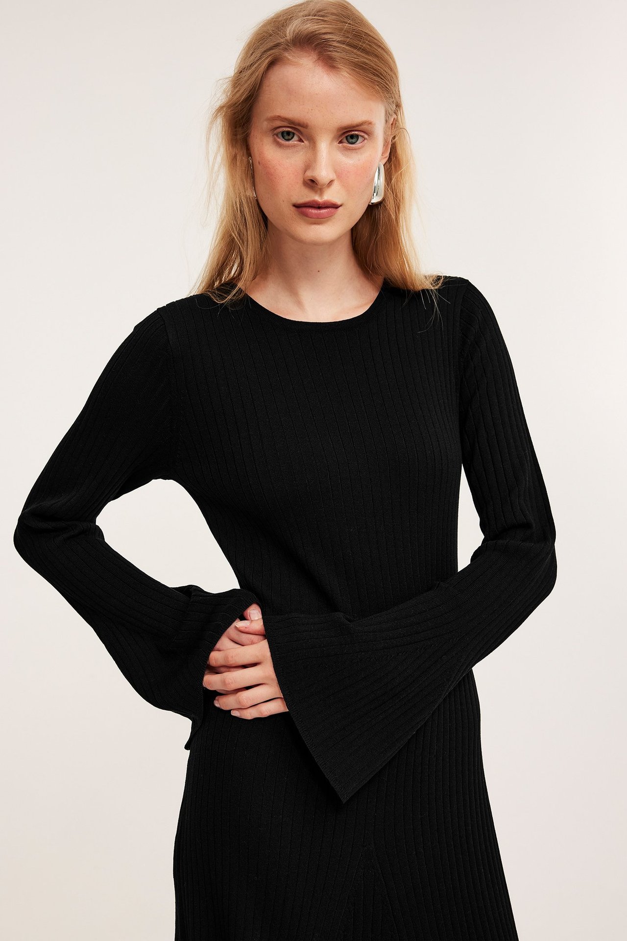 Framifrån, kvinna i svart ribbstickad klänning med utställda ärmar och silverfärgade örhängen.