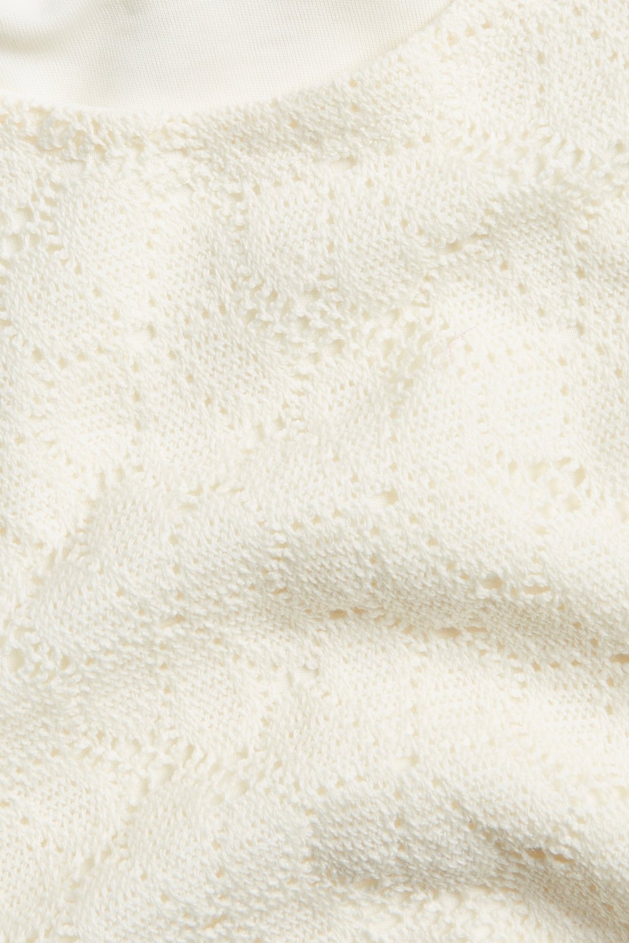 Zbliżenie na kremowy koronkowy top z krótkim rękawem, ukazujące jego wzór i widoczną podszewkę.