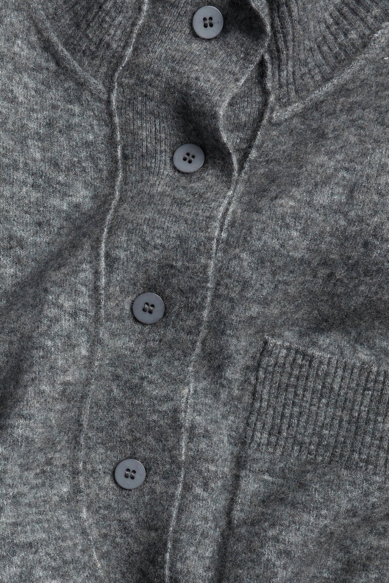 Zbliżenie na ciemnoszary kardigan z mieszanki wełny z guzikami z przodu i prążkowaną kieszenią.