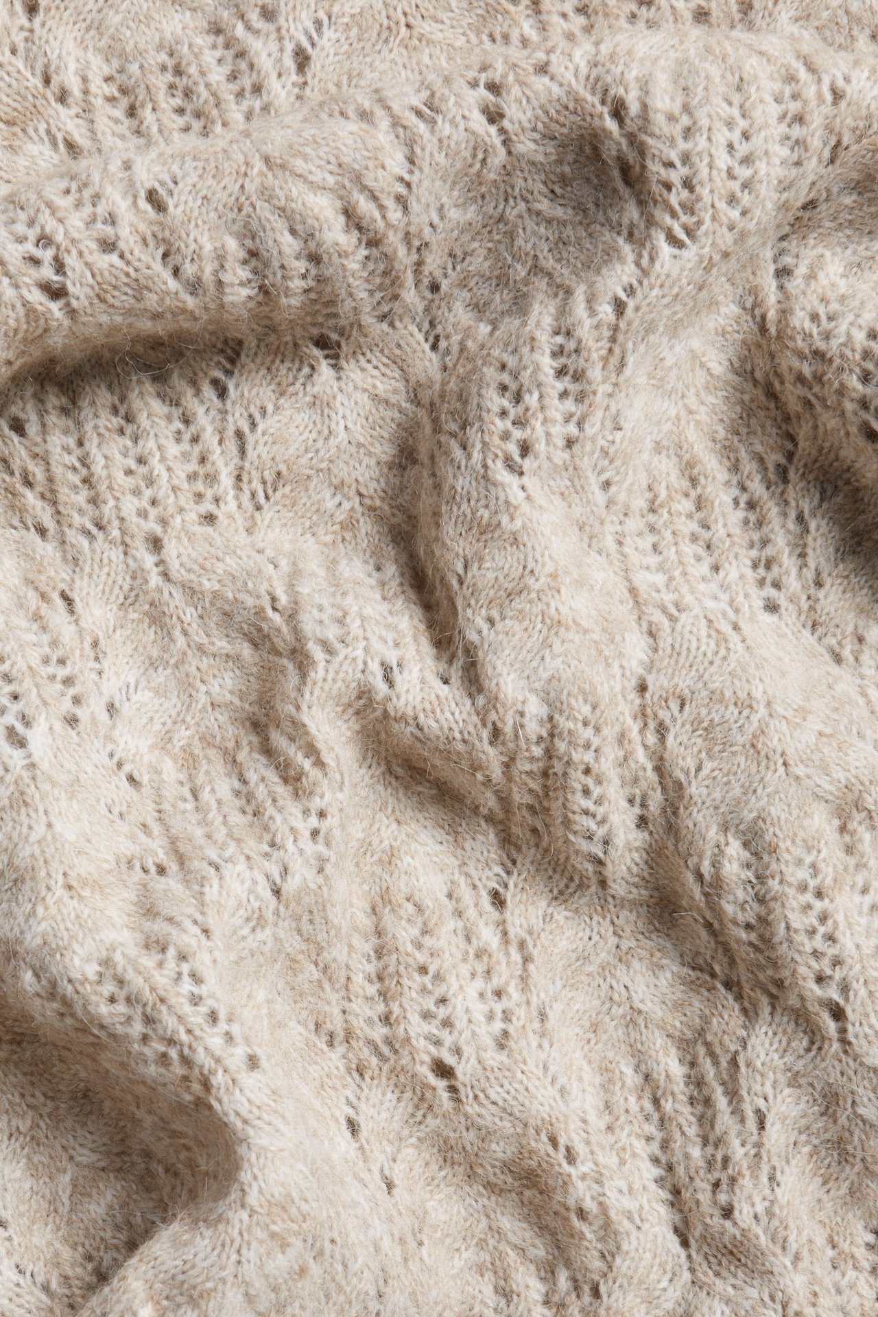 Zbliżenie na beżowy melanż dzianinowy materiał sukienki z teksturowanym wzorem.