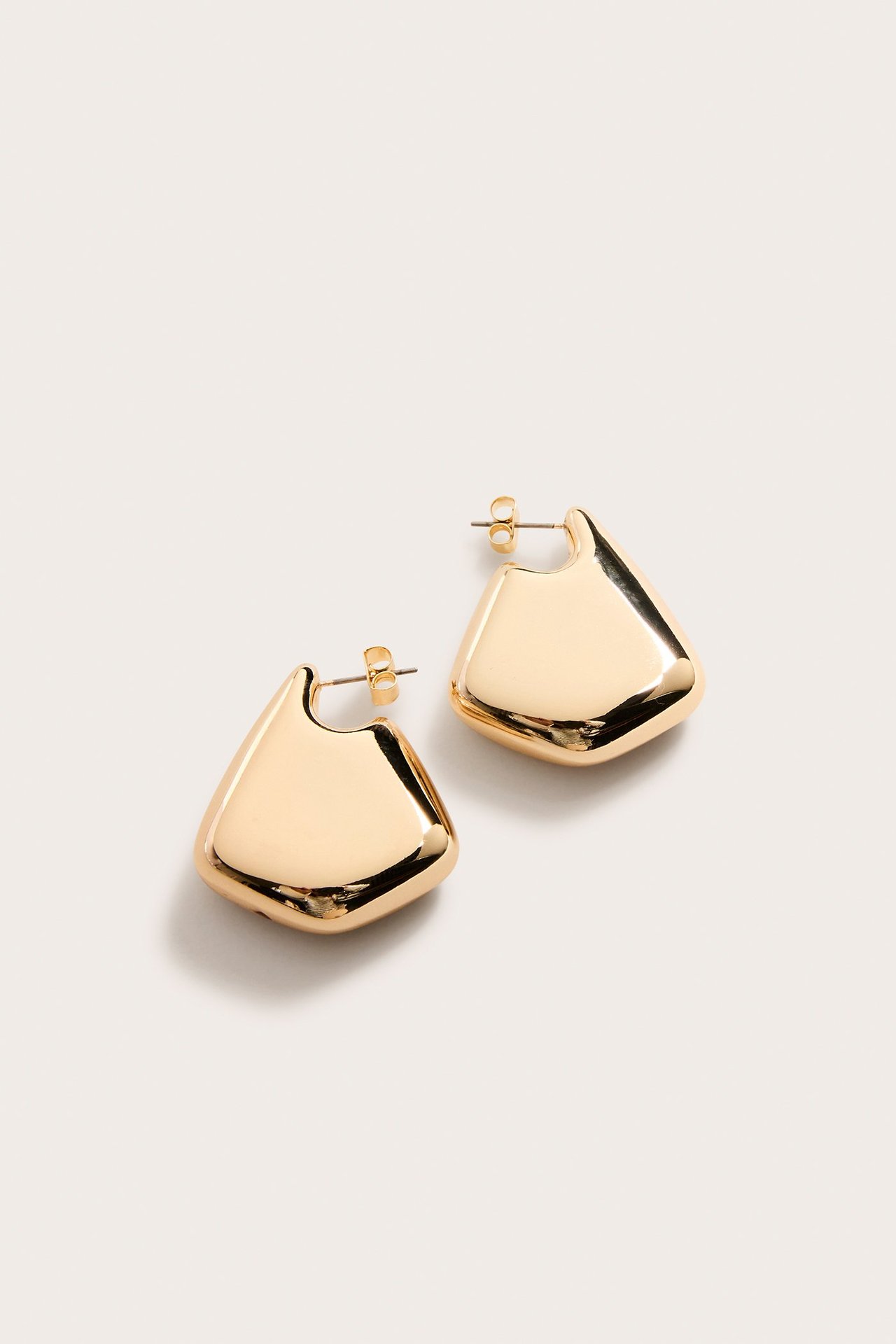 Ovenfra sett, to skinnende gullfargede, chunky, uregelmessige trapesformede øreringer med stiftlås.