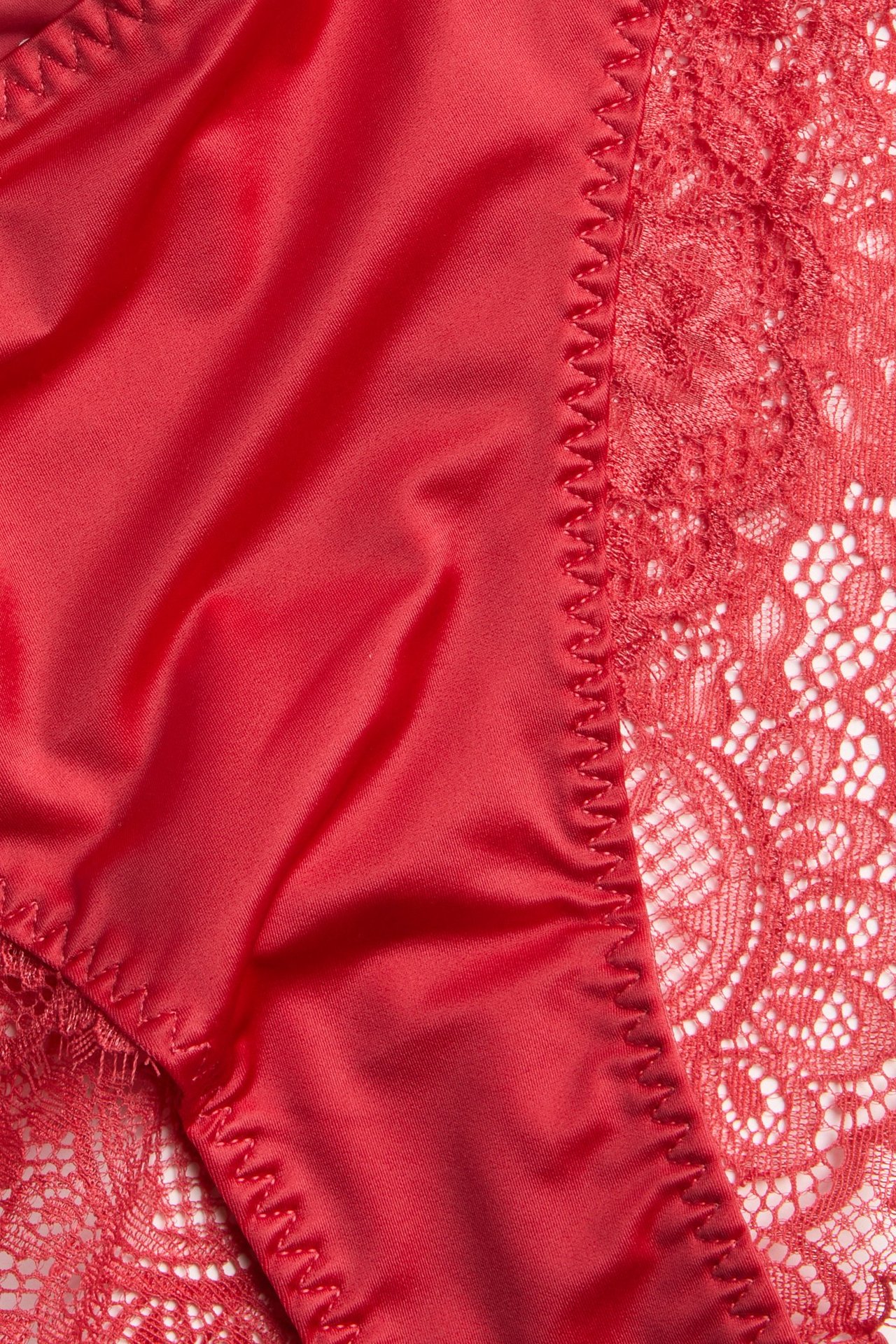 Zbliżenie czerwonych fig midi z mikrofibry, z misternymi koronkowymi panelami bocznymi i falistym szwem.