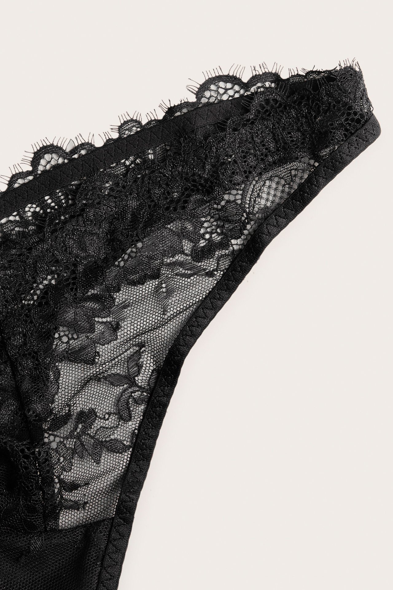 Närbild av svarta stringtrosor i spets med vågig kant, tillverkade av polyamid och elastan.