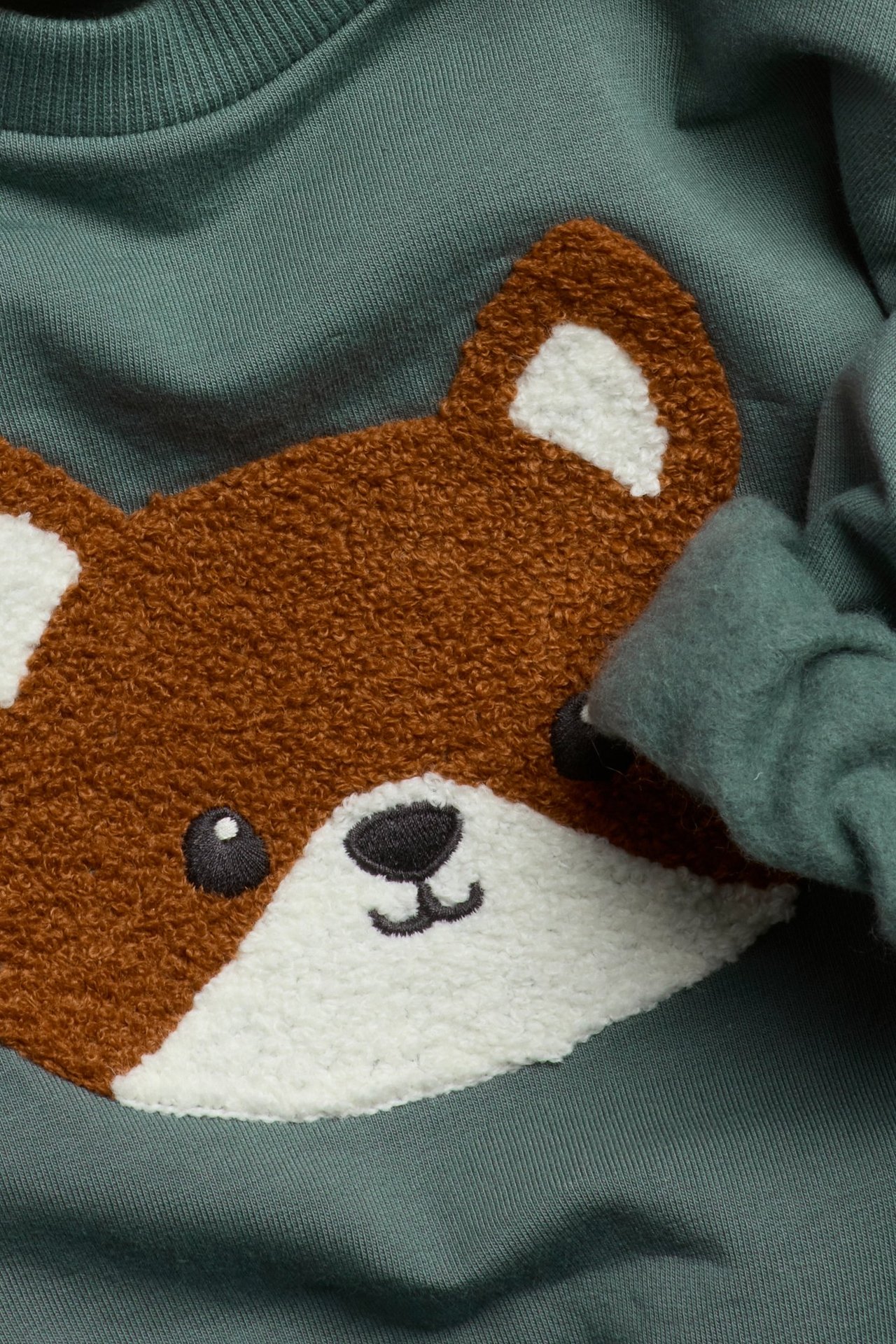 Zbliżenie na khaki zieloną bluzę niemowlęcą z brązowo-białą aplikacją lisa z froty.