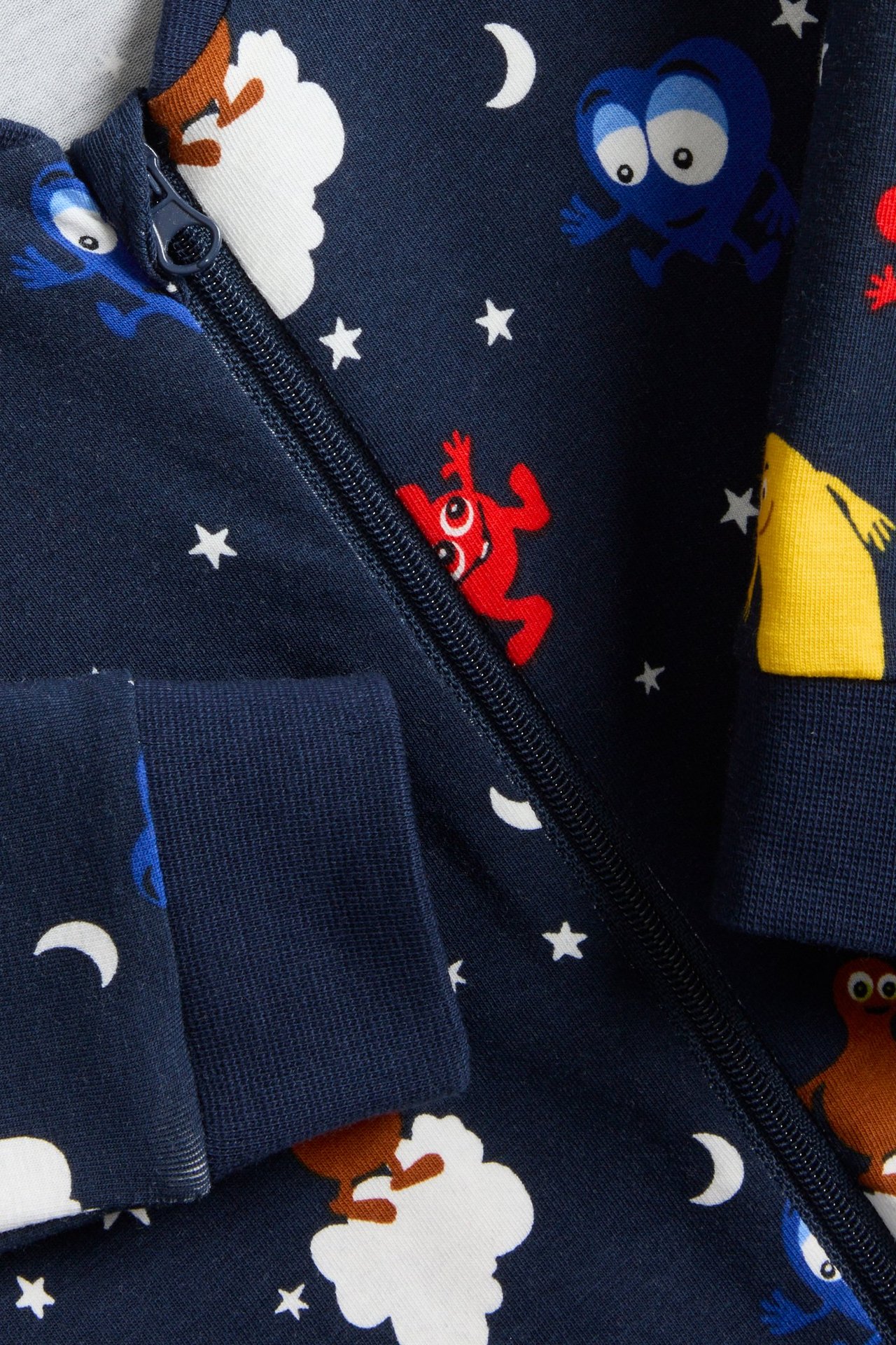 Närbild på mörkblå babypyjamas med färgglada Babblarna-figurer, stjärnor och månar, med dragkedja fram.