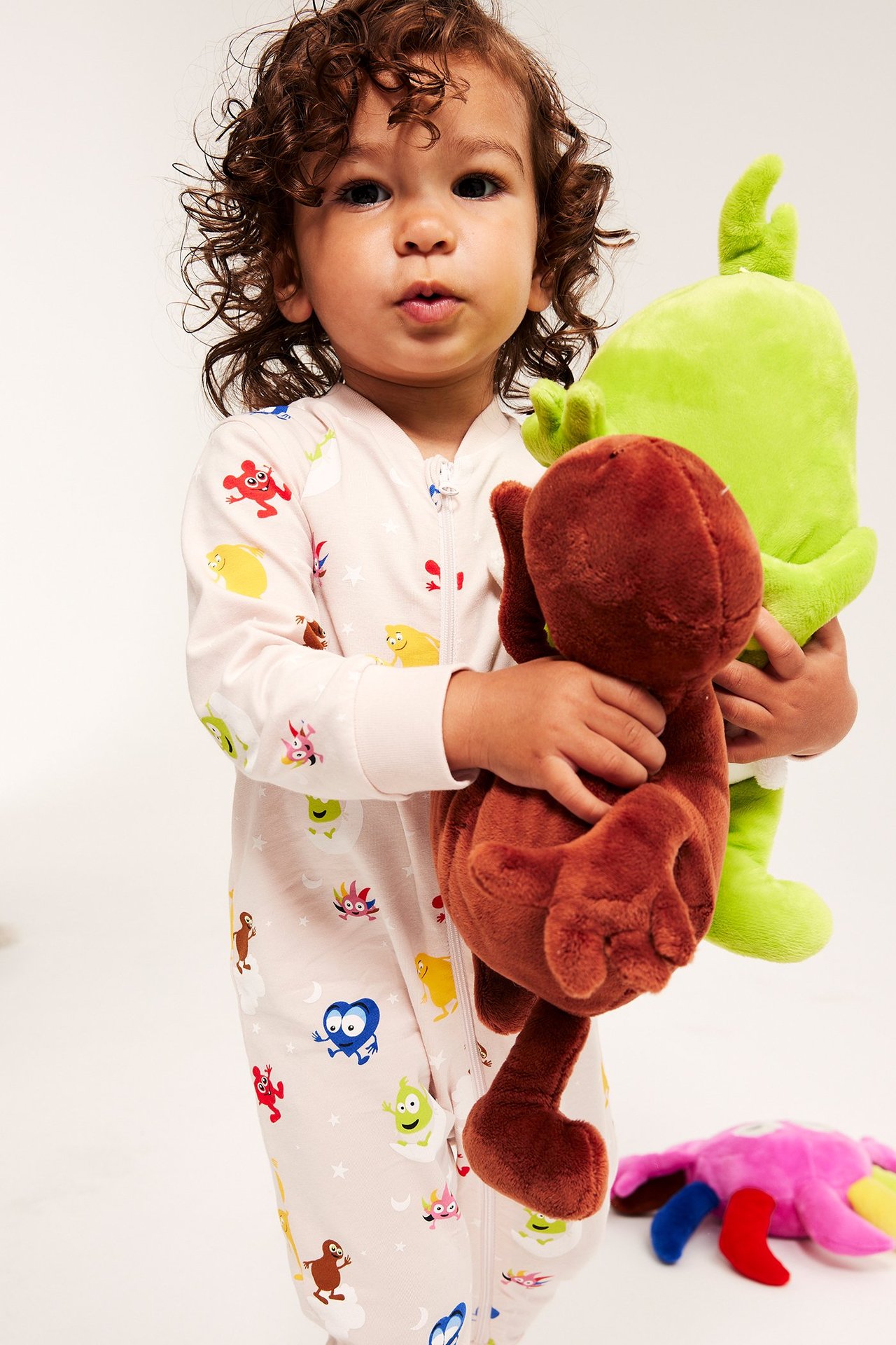 Liten flicka i babypyjamas med Babblarna-motiv, håller stora plushdjur.