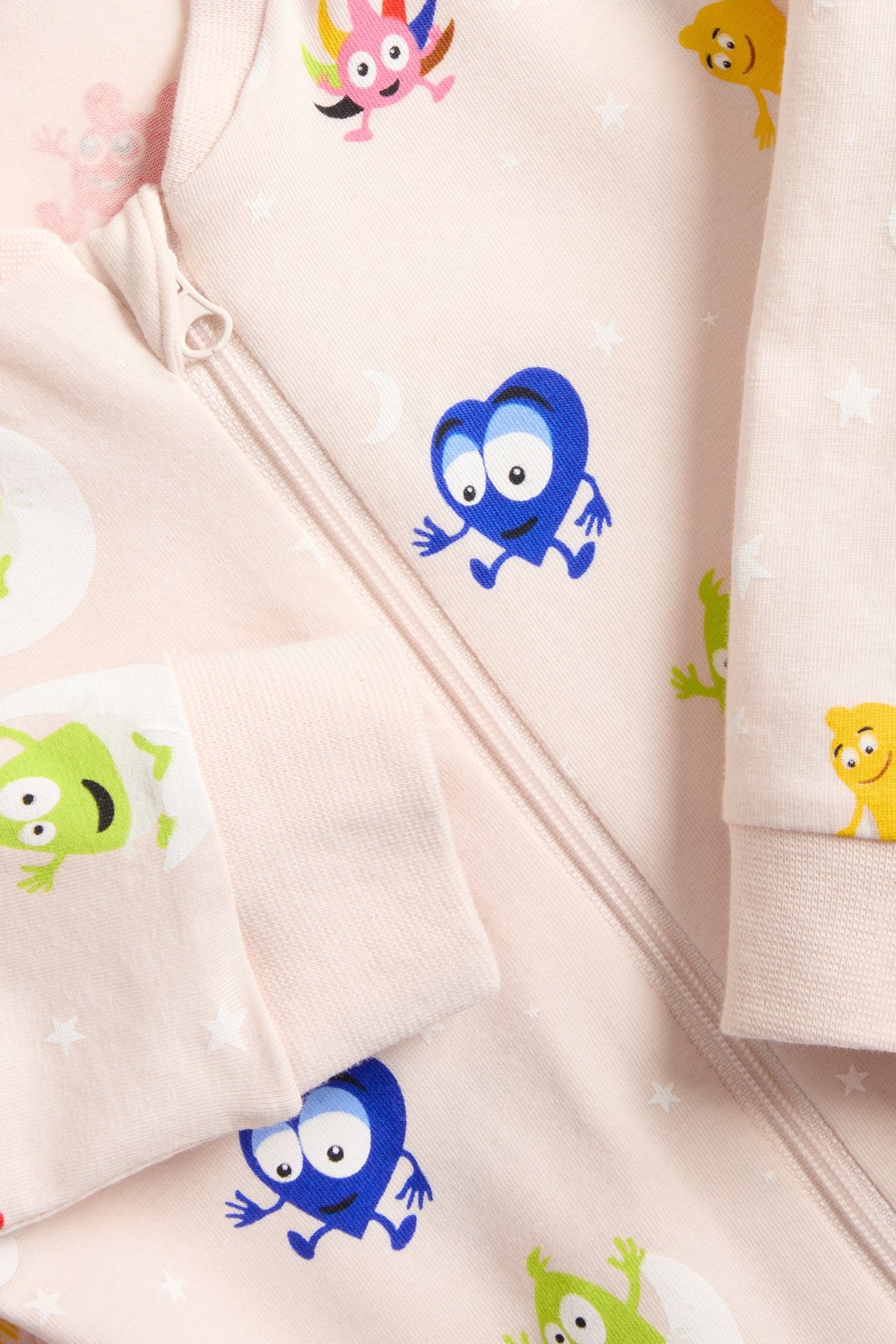 Zbliżenie różowego, wzorzystego pajacyka niemowlęcego z postaciami Babblarna, białymi gwiazdkami i zamkiem błyskawicznym.