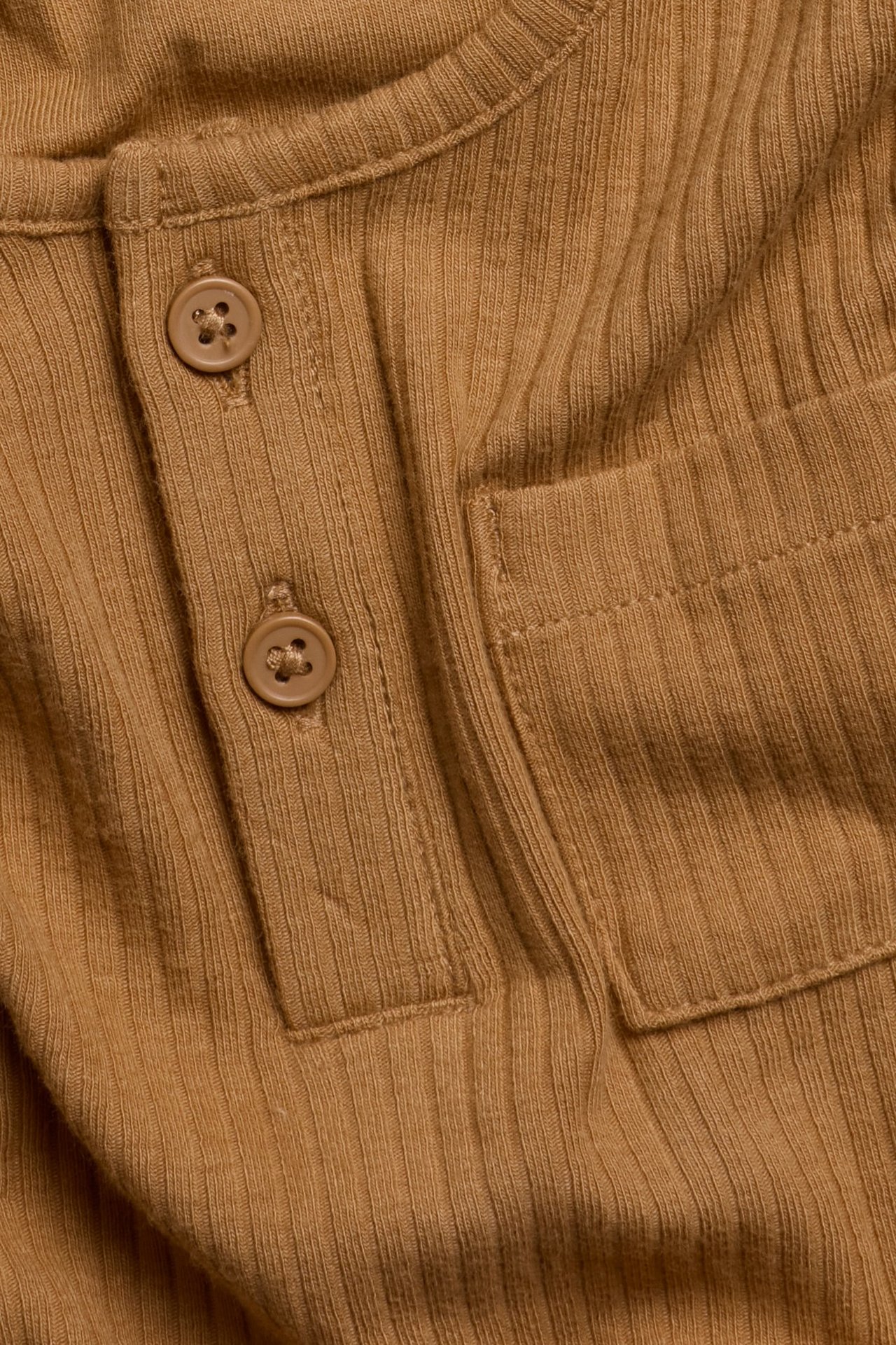 Zbliżenie brązowego prążkowanego topu z długim rękawem, z guzikami z przodu i kieszenią na piersi.