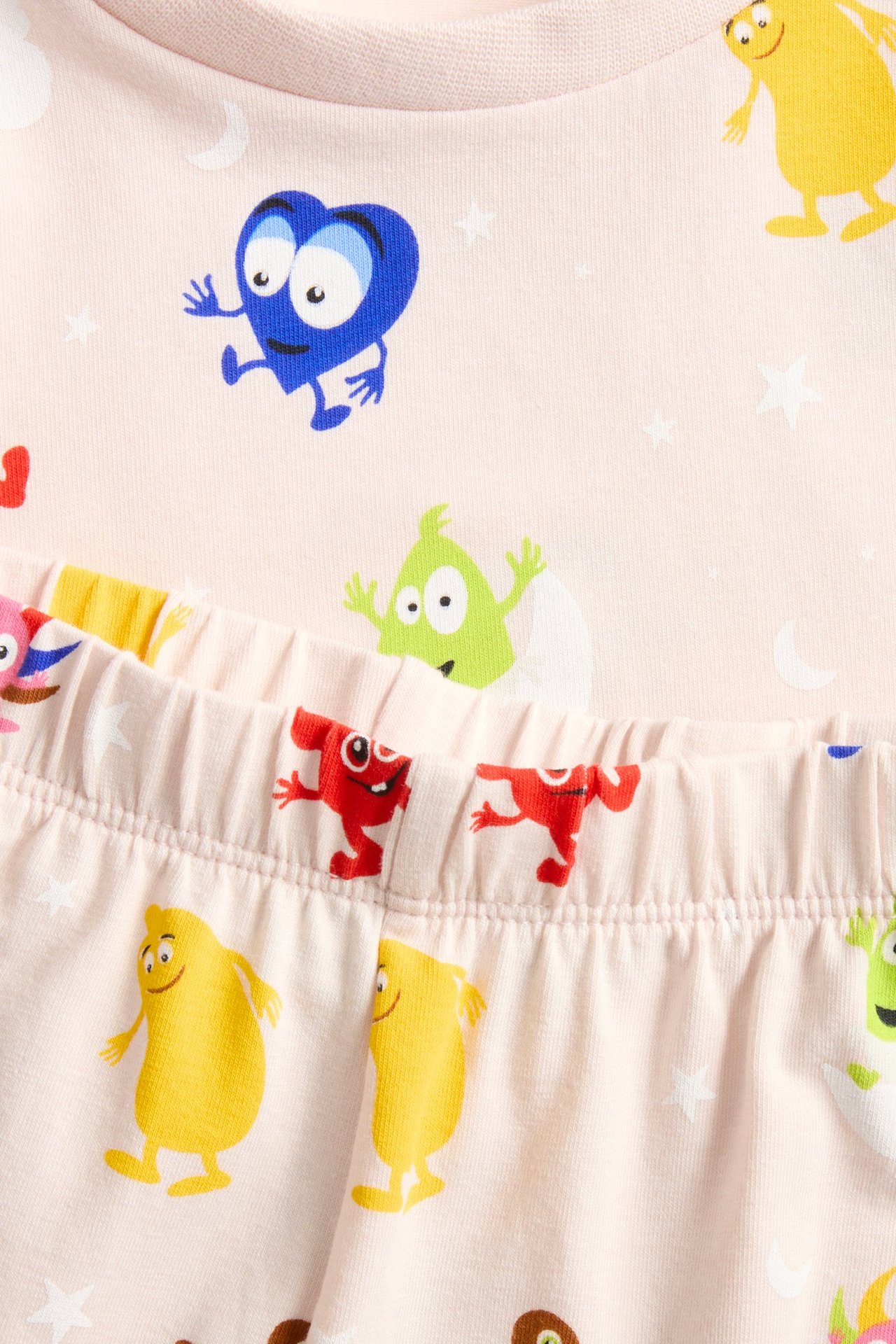 Zbliżenie różowej, wzorzystej piżamy dziecięcej z postaciami Babblarna, gwiazdkami i księżycami.