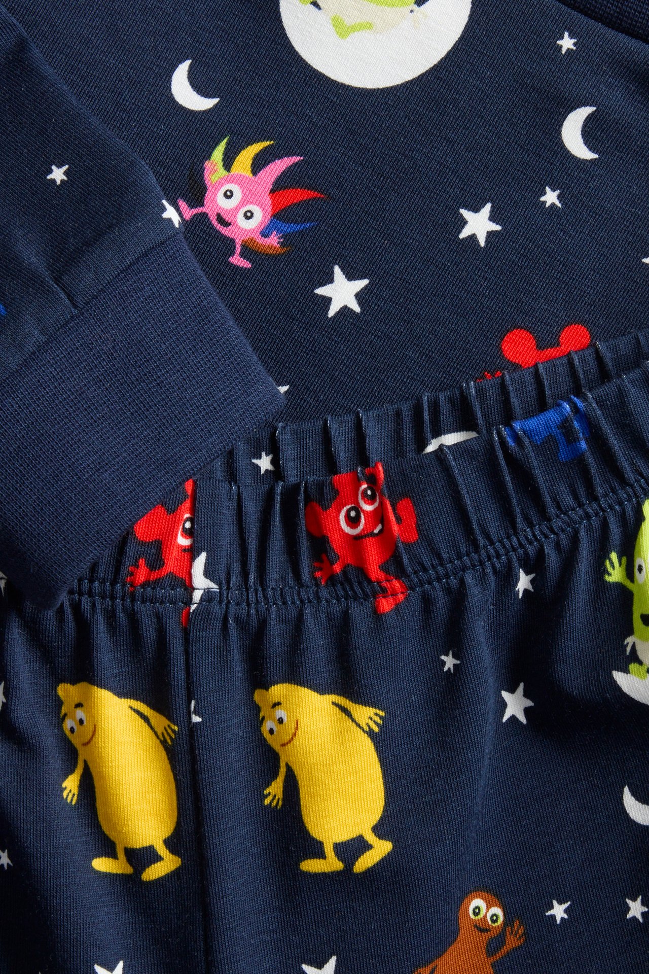 Närbild av mörkblå mönstrad barnpyjamas i bomull med färgglada Babblarna-figurer, stjärnor och månar.