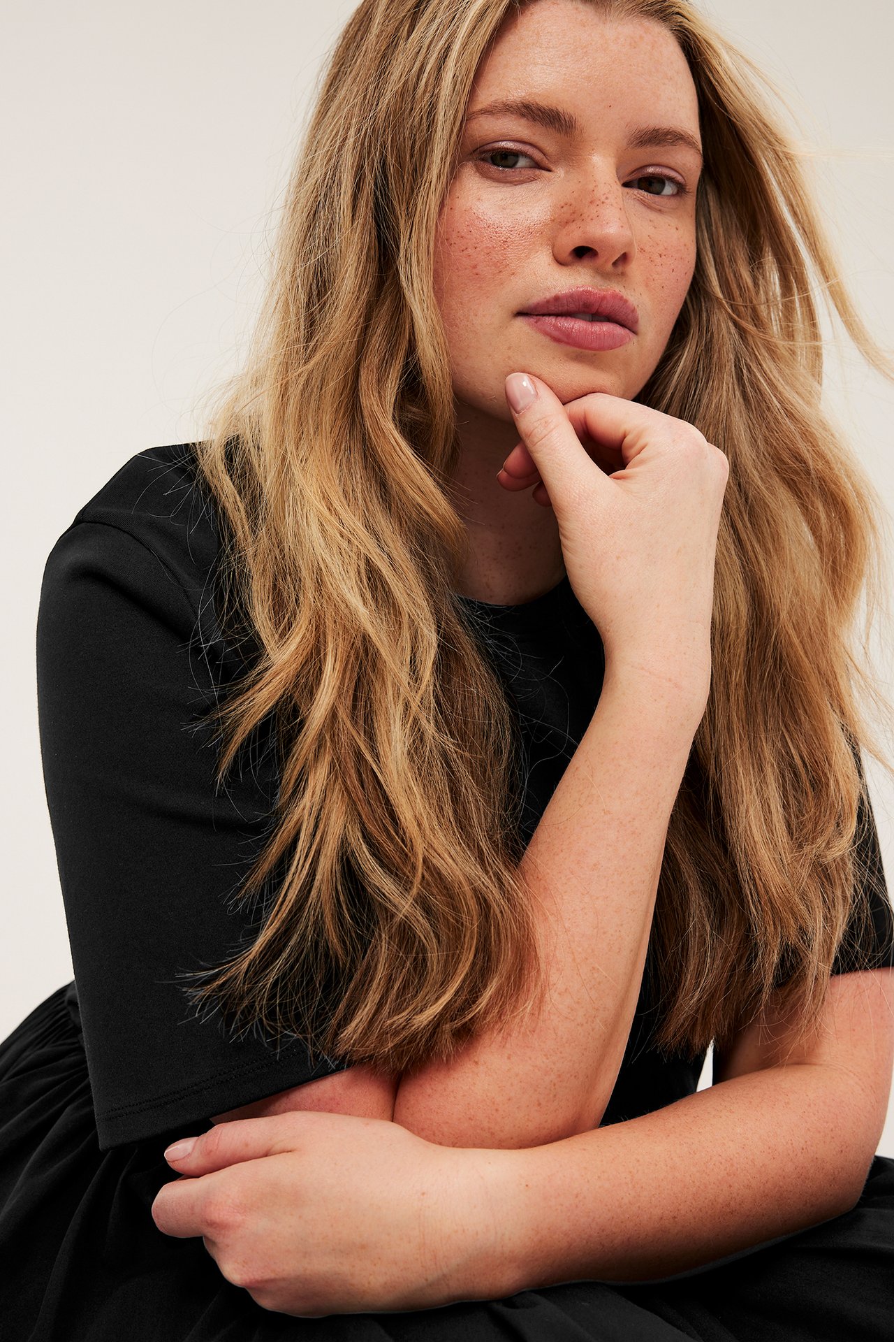 Närbild av en kvinna i svart rundhalsad klänning med korta jerseyärmar och poplinkjol.