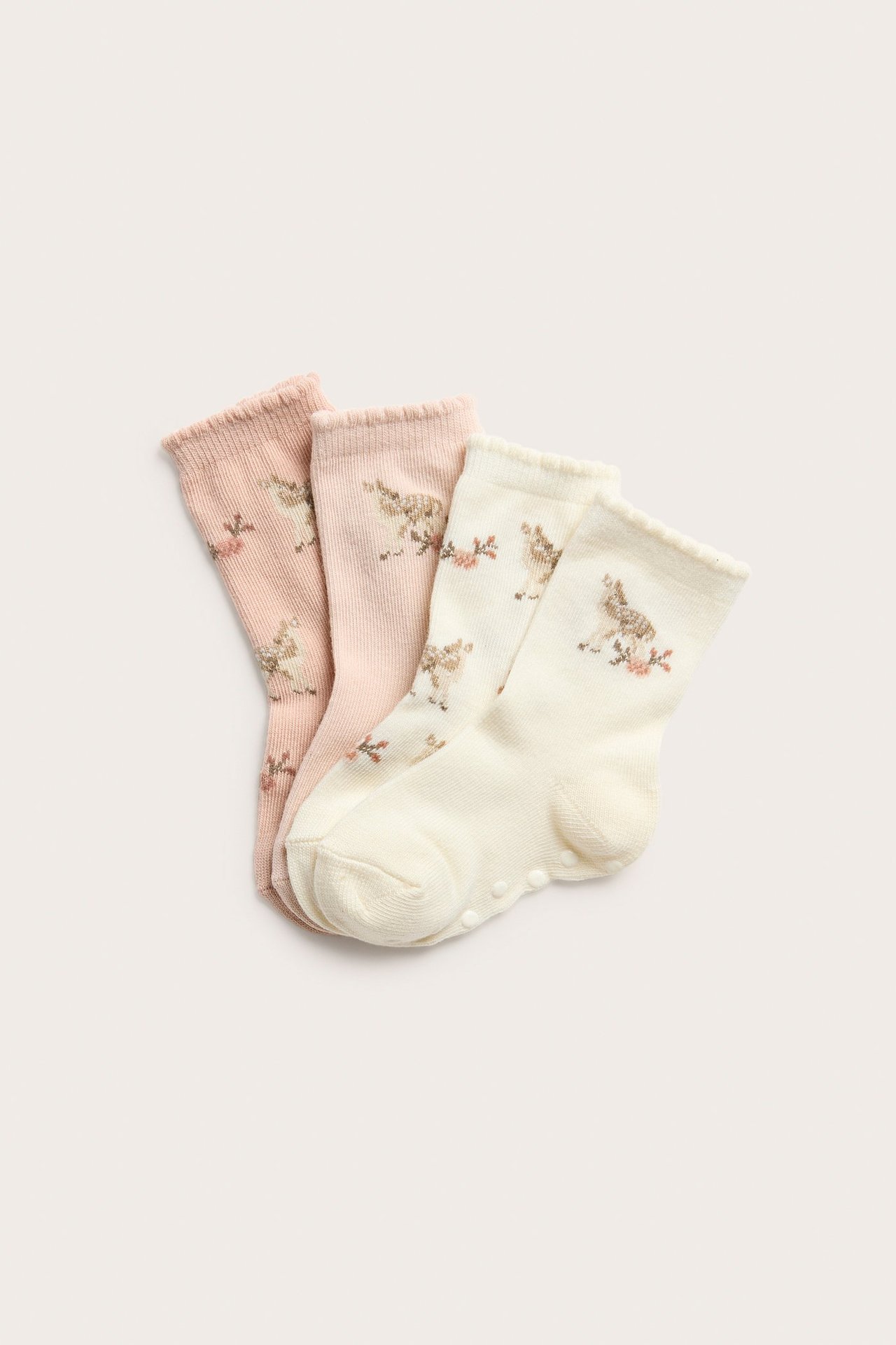 Ovenfra: Fire par babystrømper i lys rosa og kremhvit med hjorte- og blomstermønster, antiskli på sålene.