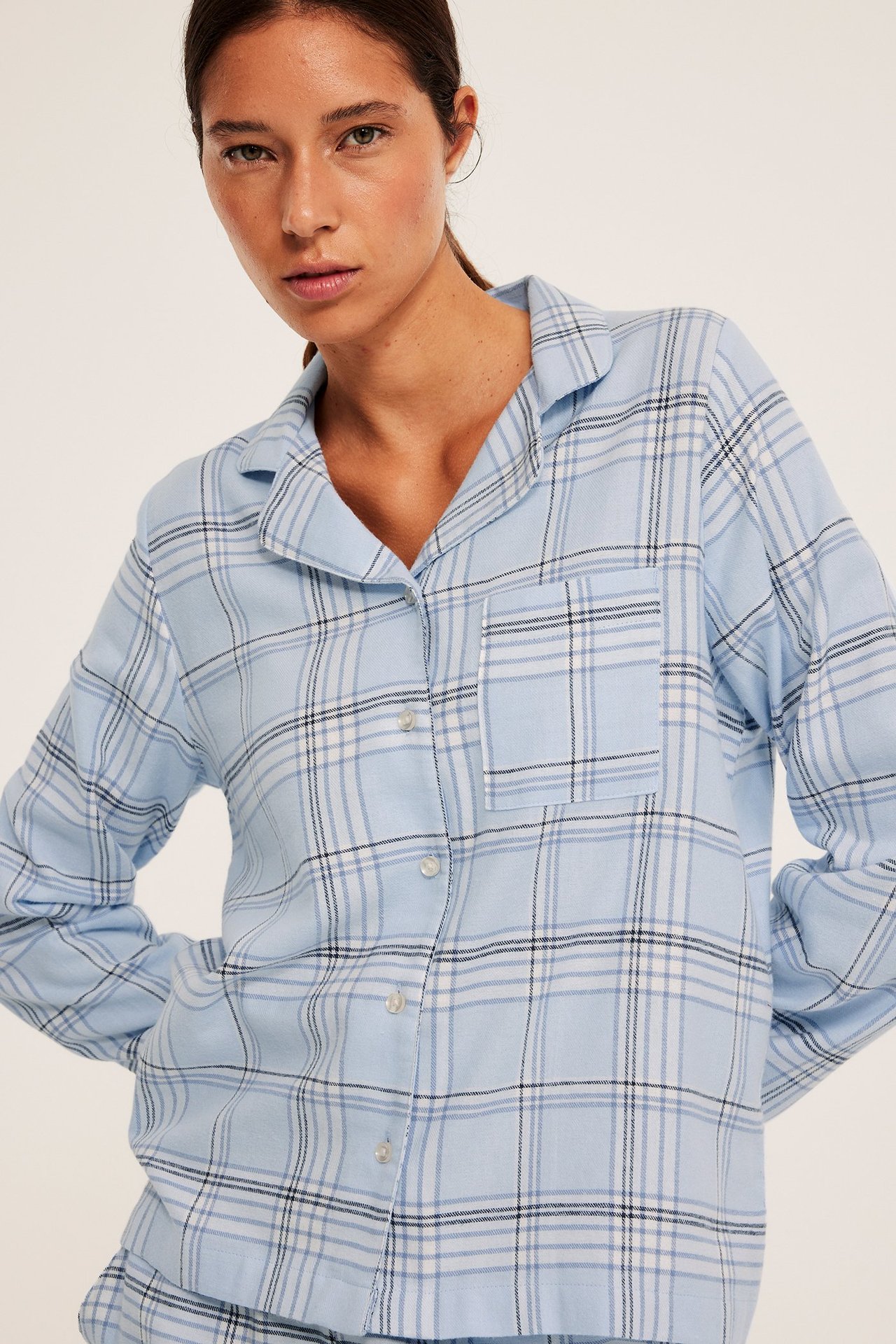 Nainen sinisissä ruudullisissa flanelliyöpukumissa, kaulus, rintatasku, ja sivutaskut.