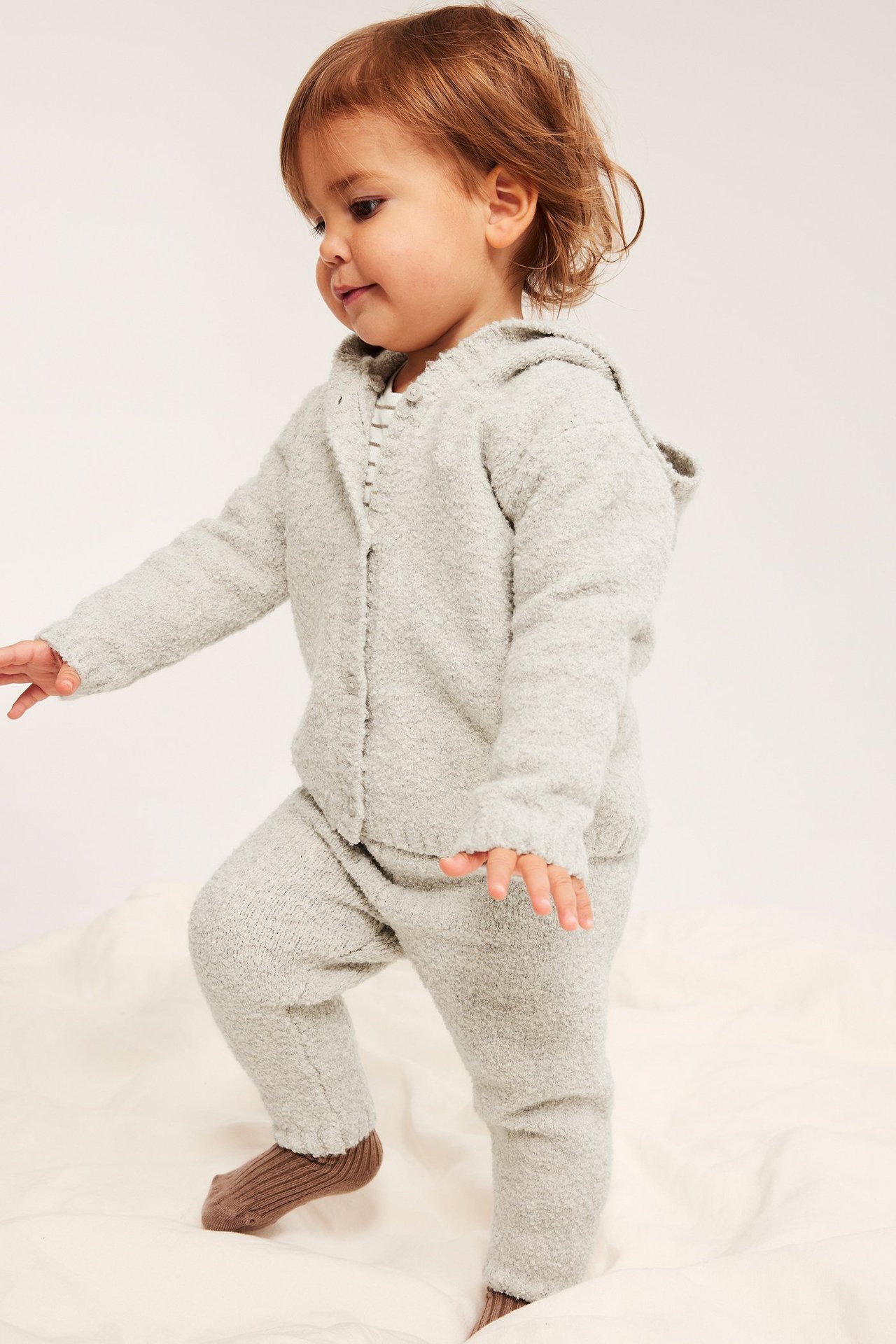 Sidebilde: baby i lyse melange bouclé-leggings, matchende hettejakke og brune sokker.