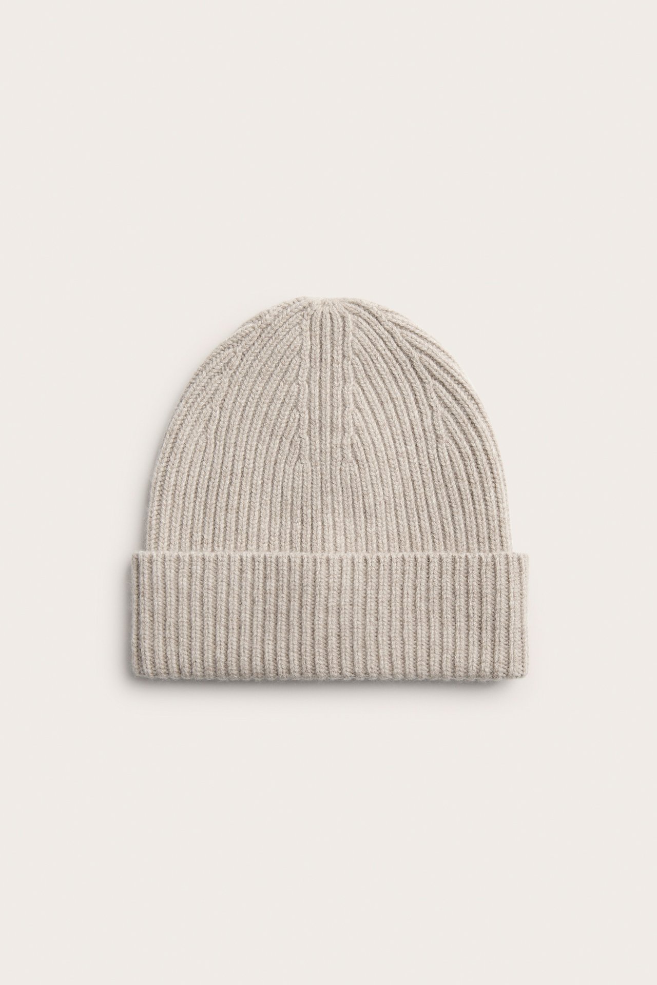 Framifrån, en beige melerad ribbad mössa i ull med vikt kant.