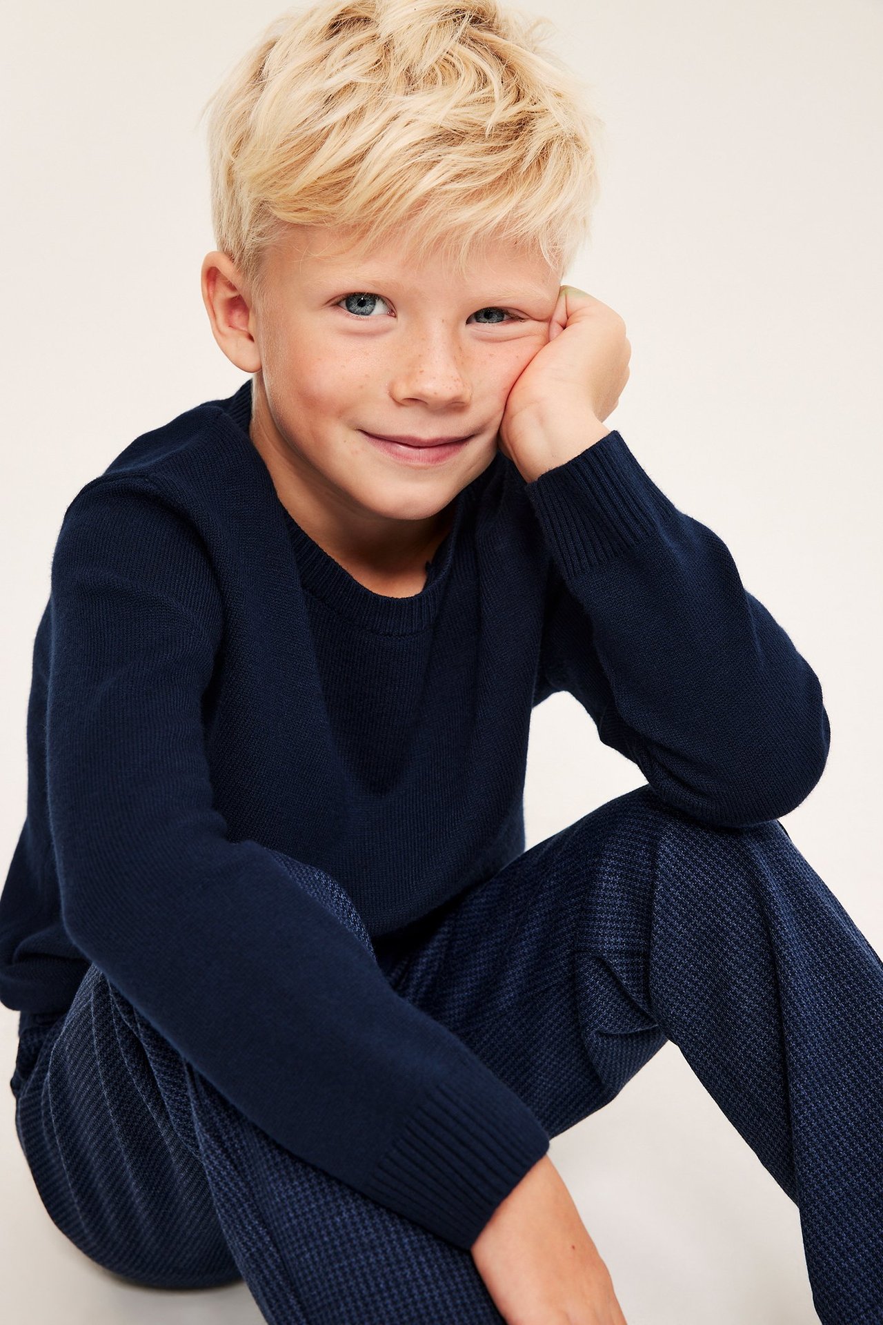 Framsida: Pojke i mörkblå stickad tröja och mörkblå mönstrade byxor.