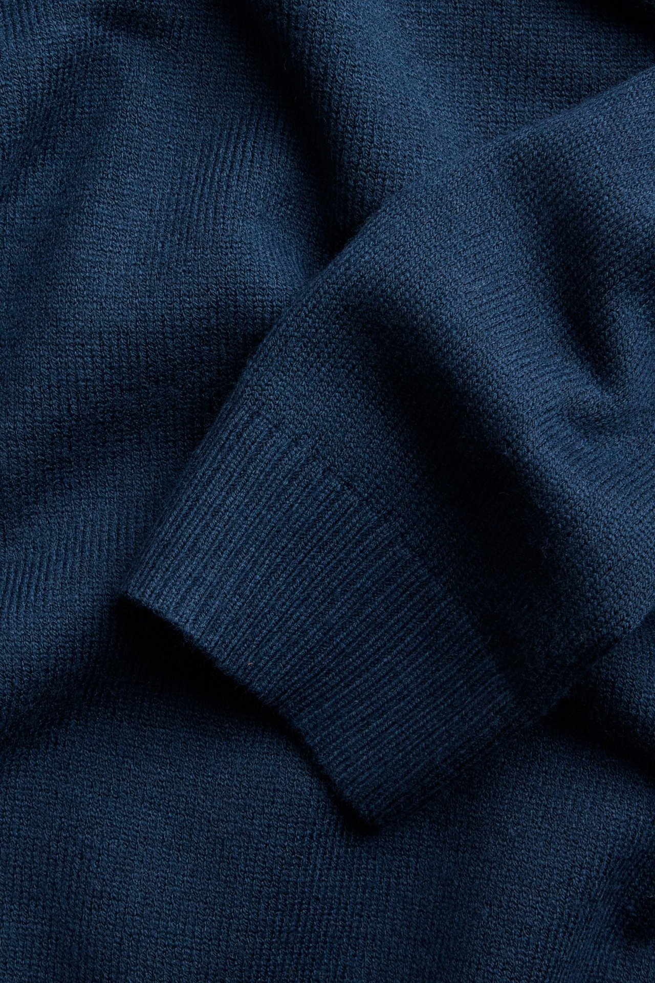 Zbliżenie na ciemnoniebieski sweter z dzianiny z widocznym ściągaczem.