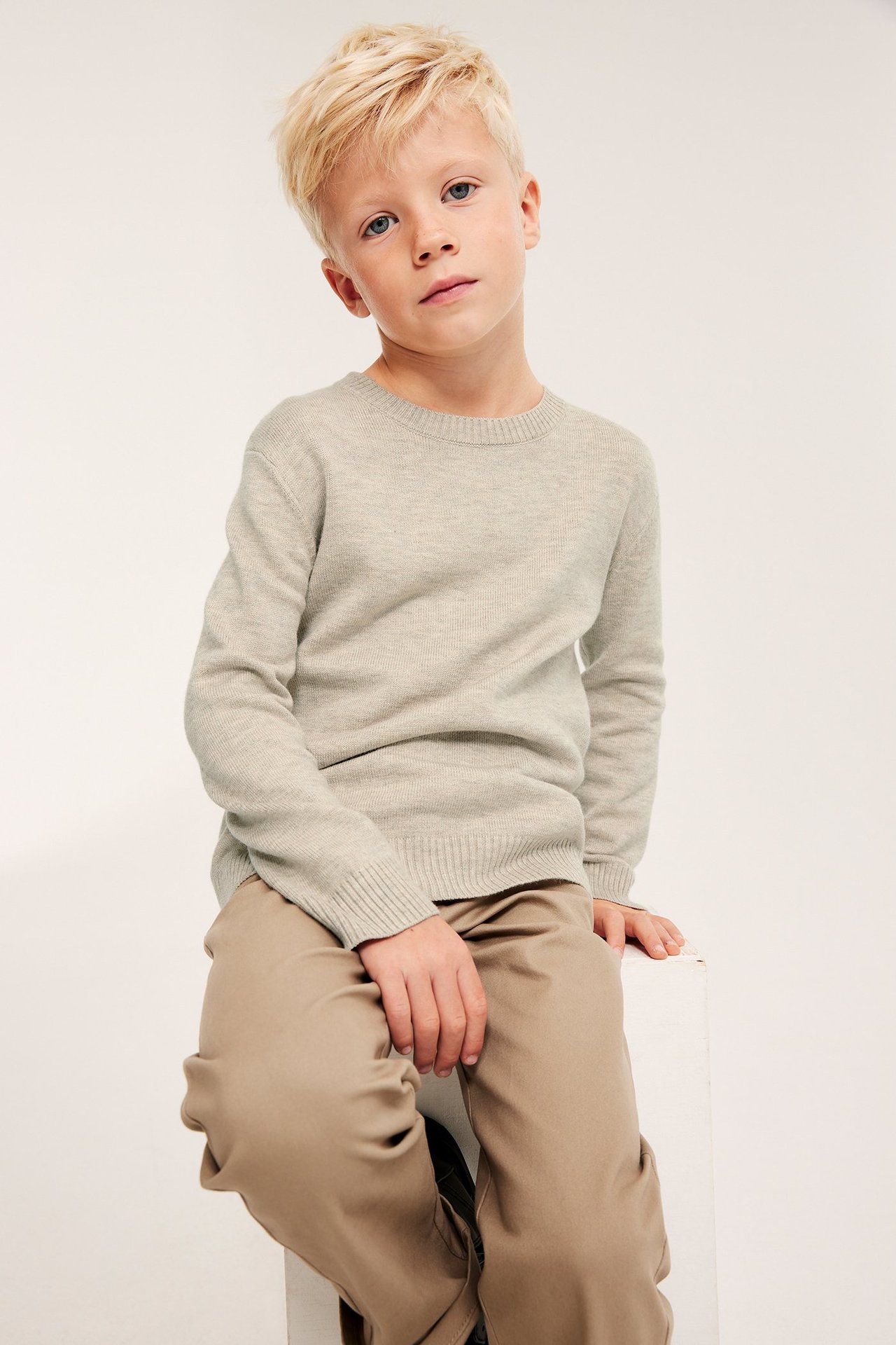 Barn man i beige melange stickad tröja med ribb i hals, ärmavslut och nederkant.