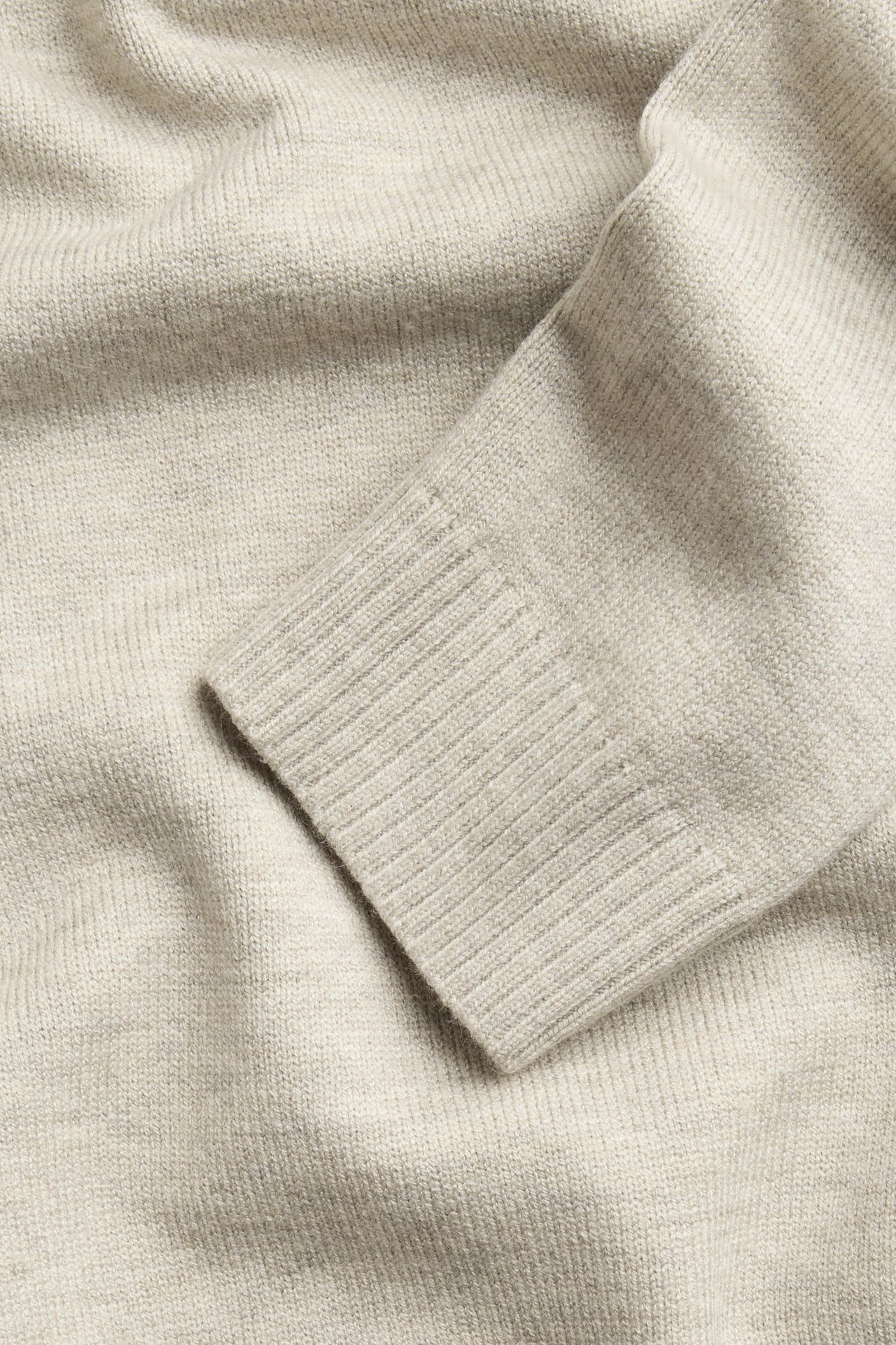 Zbliżenie na beżowy melanżowy sweter dzianinowy, ukazujące ściągacz rękawa.