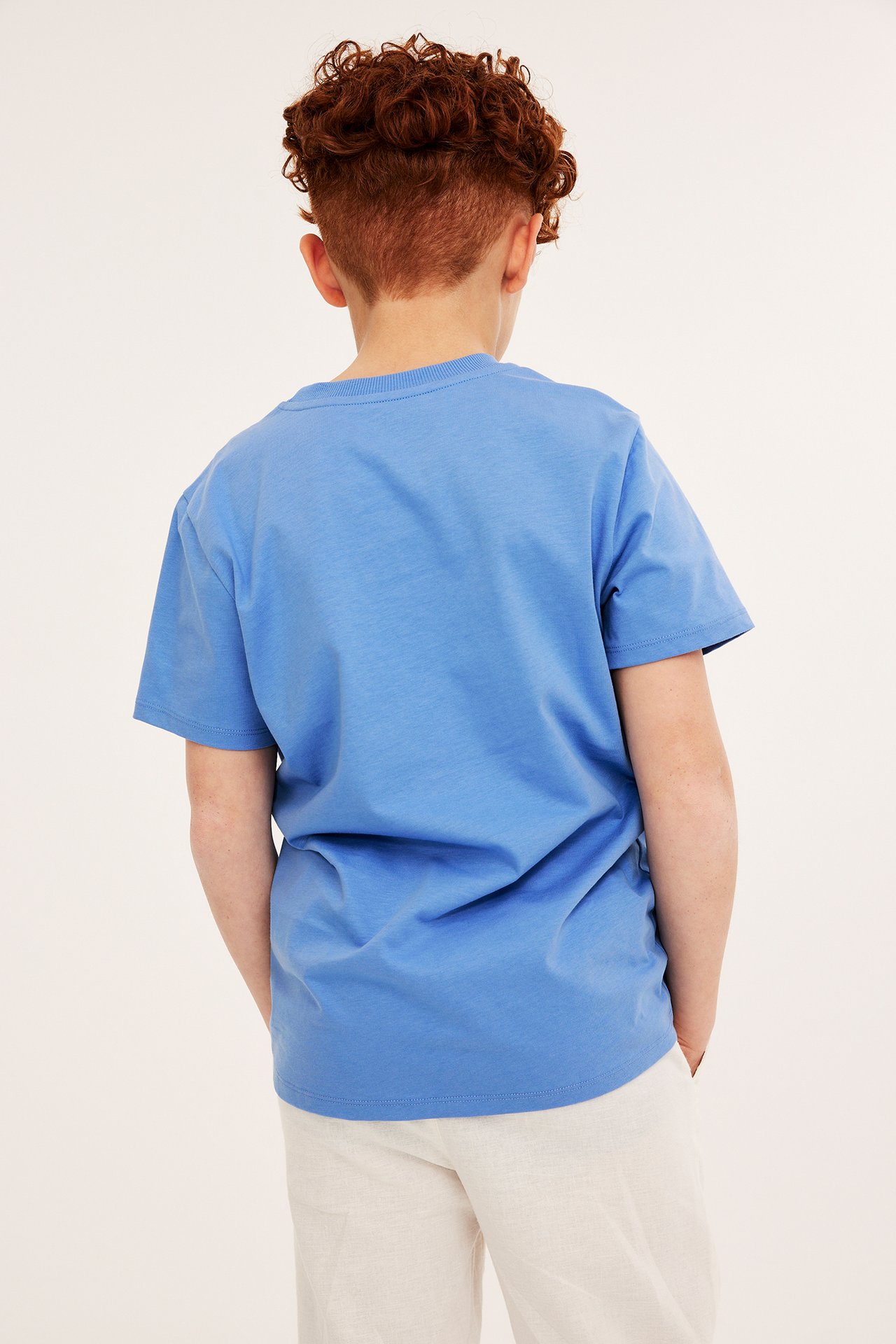 Bakifrån, ett barn i en blå bomulls-t-shirt och ljusbeige byxor.