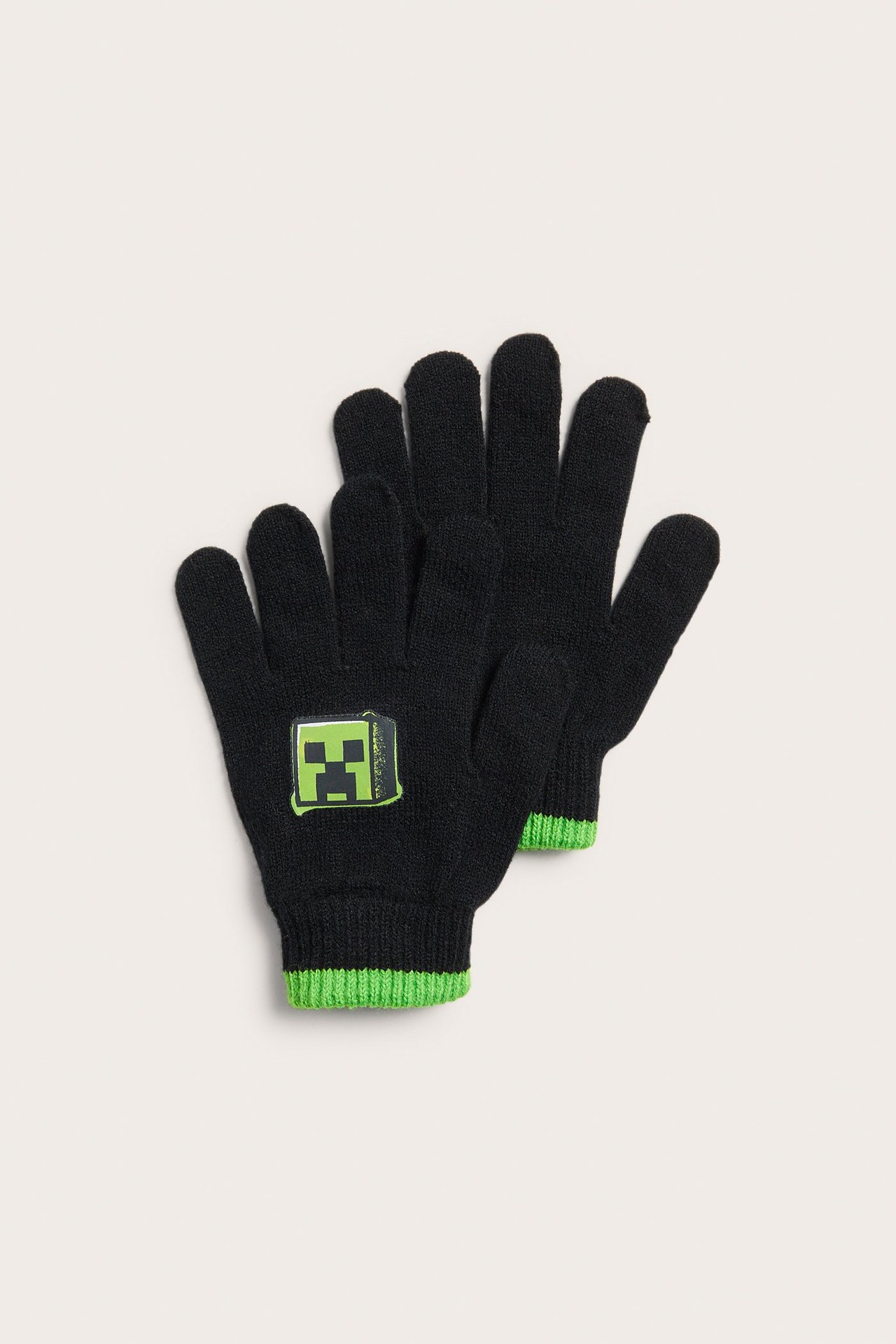 Framifrån: svarta stickade barnfingervantar med grönt Minecraft Creeper-tryck och gröna ribbade muddar.