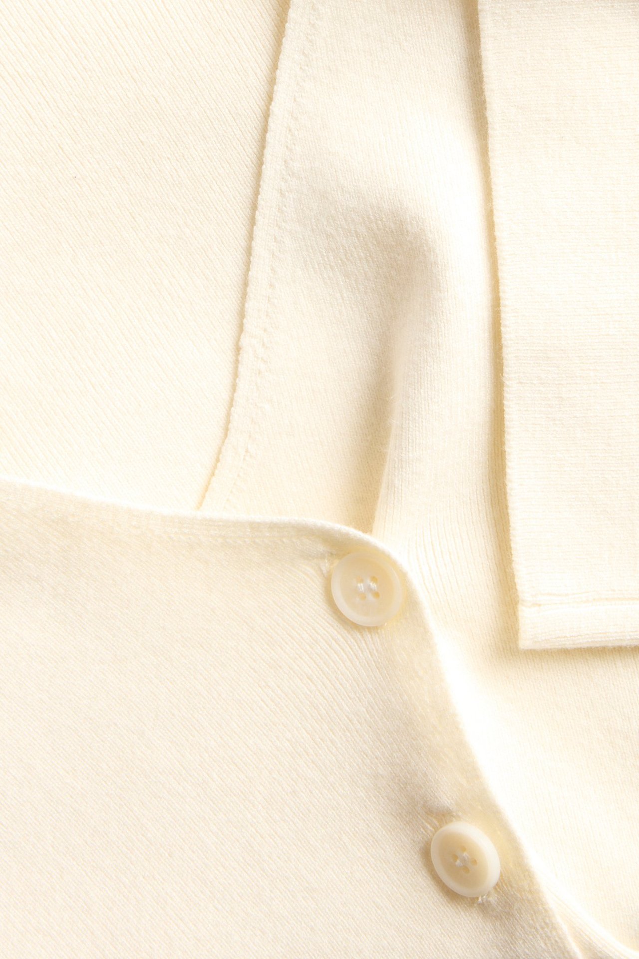 Zbliżenie na kremowy dzianinowy kardigan z dwoma widocznymi guzikami.