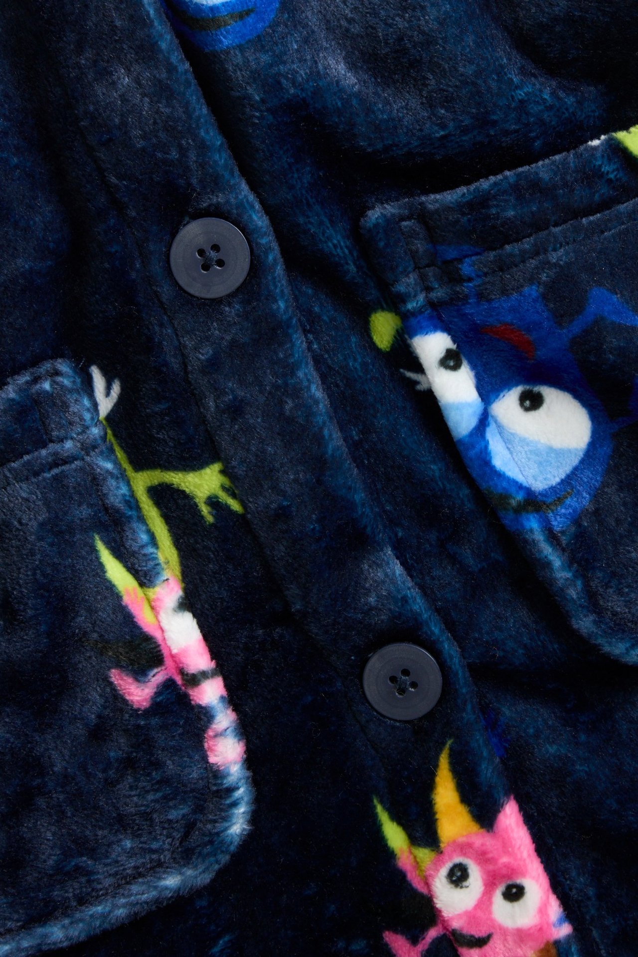 Nærbilde, forfra: mørkeblå mønstret fleece-morgenkåpe for baby, med to knapper og lommer.