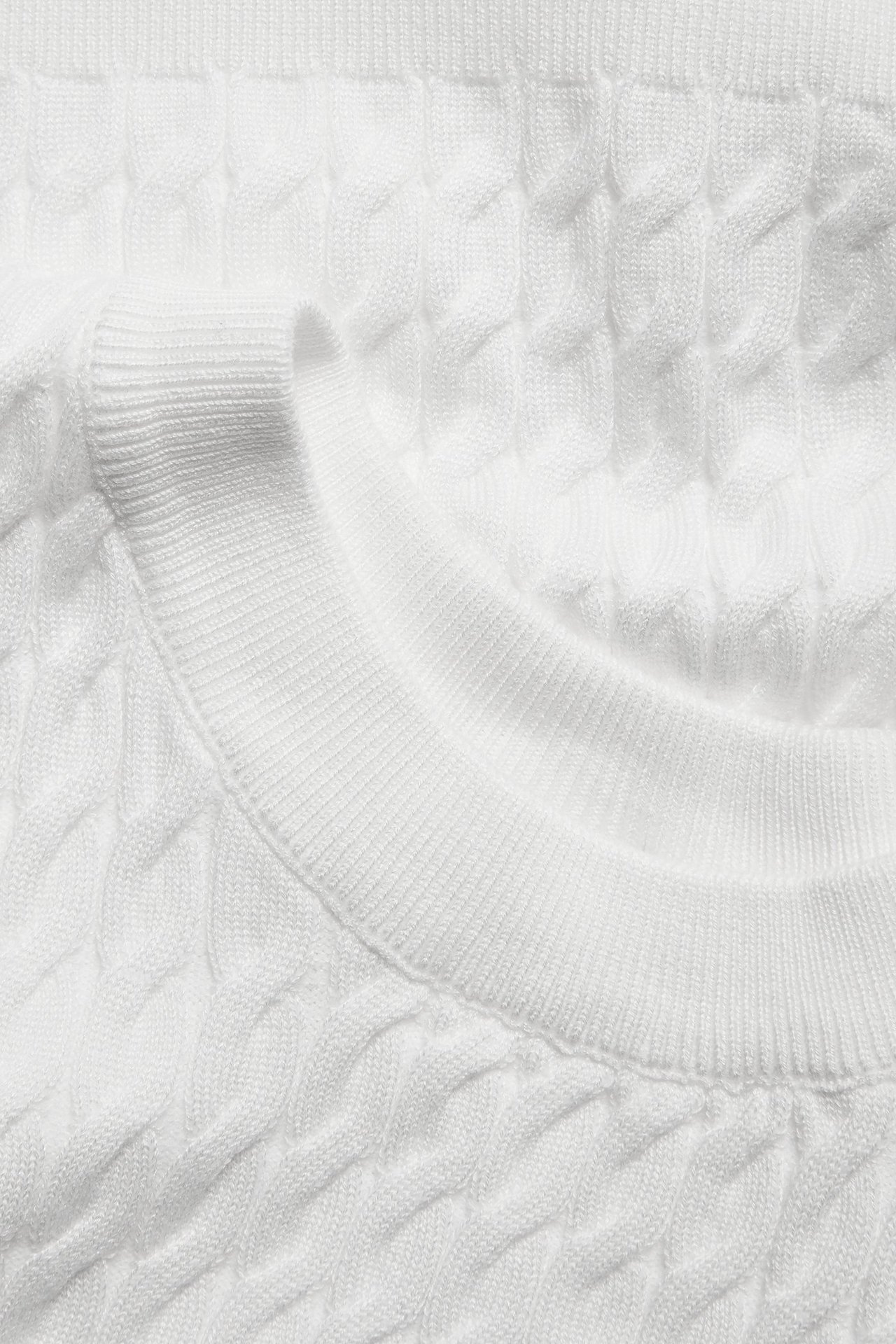 Zbliżenie na kremowy sweter z warkoczowym splotem i prążkowanym okrągłym dekoltem.