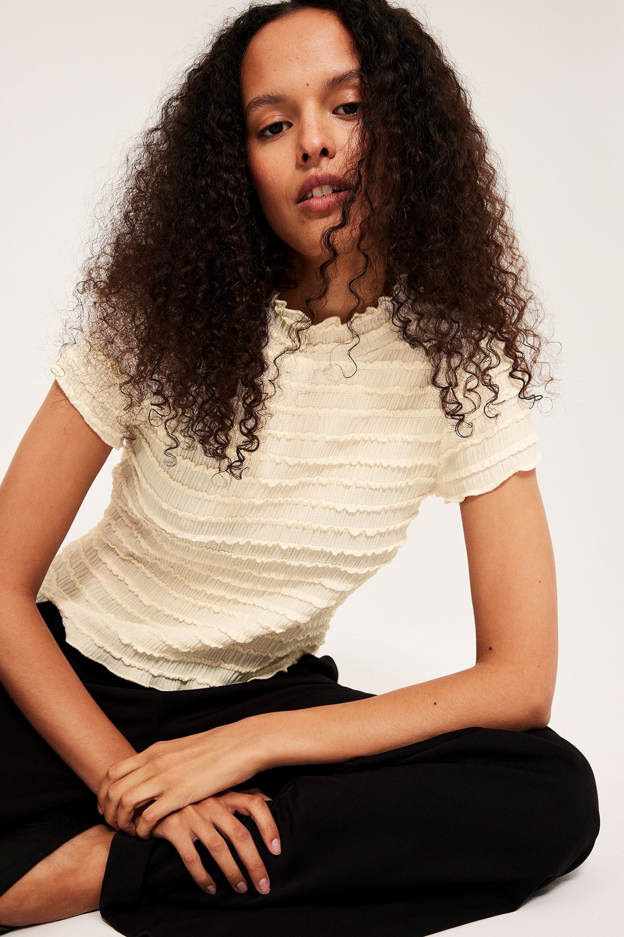 Widok z przodu, kobieta w kremowym strukturalnym topie z krótkim rękawem i czarnych spodniach.