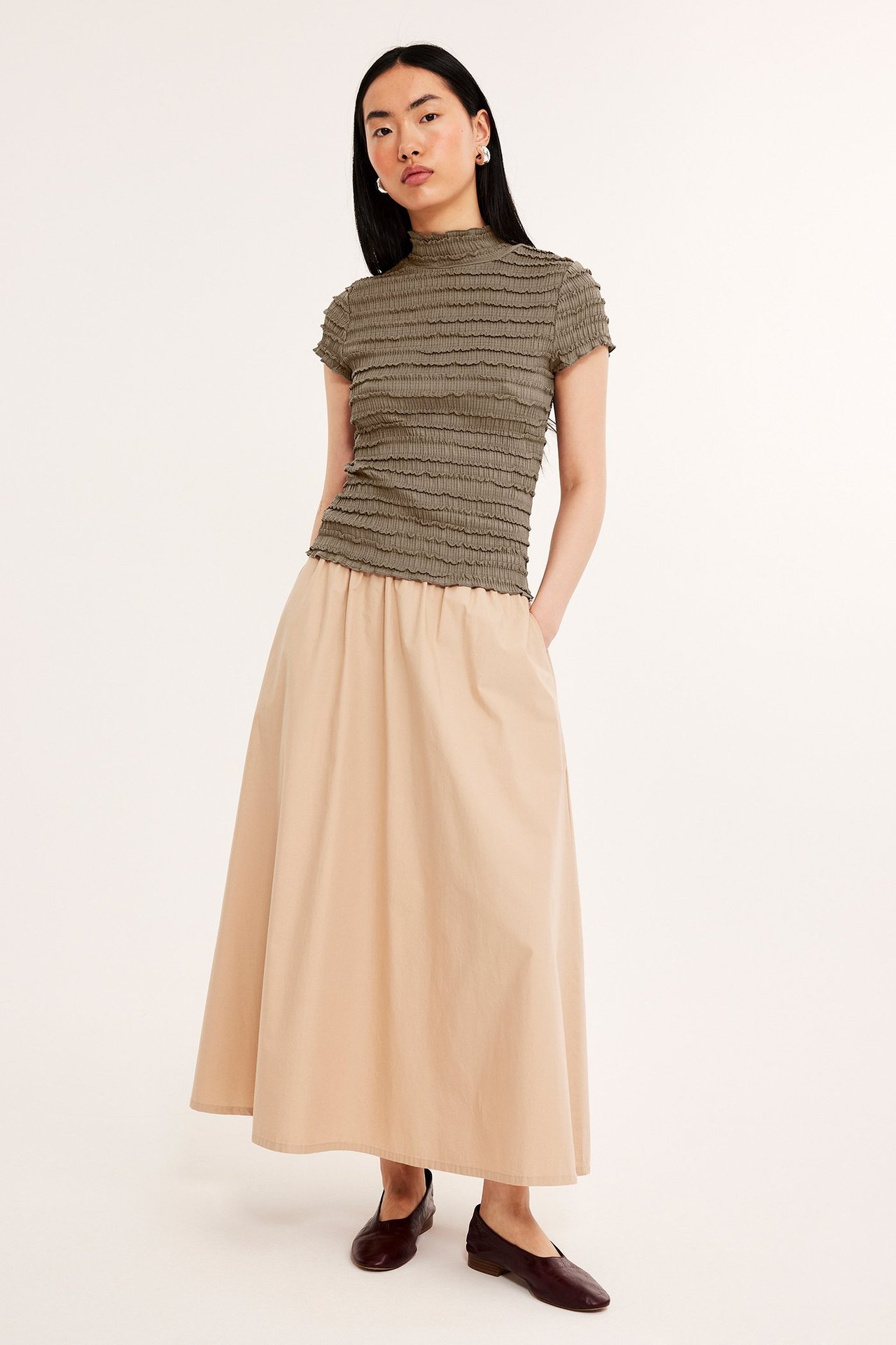 Forfra: kvinne i khaki strukturert kortermet topp, beige maxiskjørt og mørkebrune flate sko.
