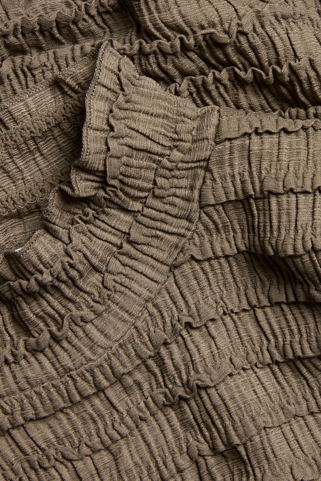 Zbliżenie brązowego, strukturalnego materiału topu z marszczonym wzorem.