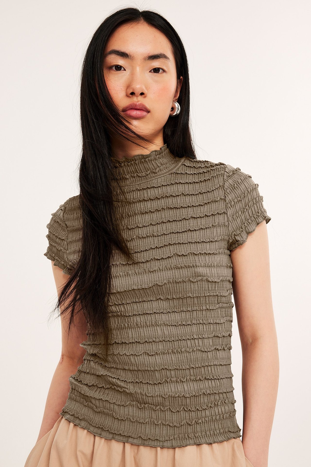 Widok z przodu: Kobieta w dopasowanym brązowym strukturalnym topie z krótkim rękawem, stójką i jasnobeżowym dołem.