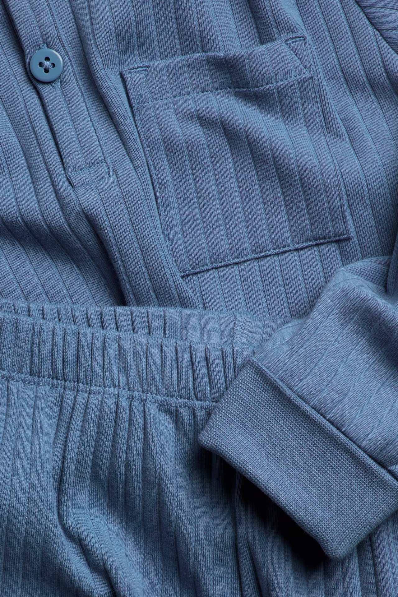 Zbliżenie niebieskiej prążkowanej piżamy, pokazujące guzik, kieszeń, elastyczny pas i ściągacze.