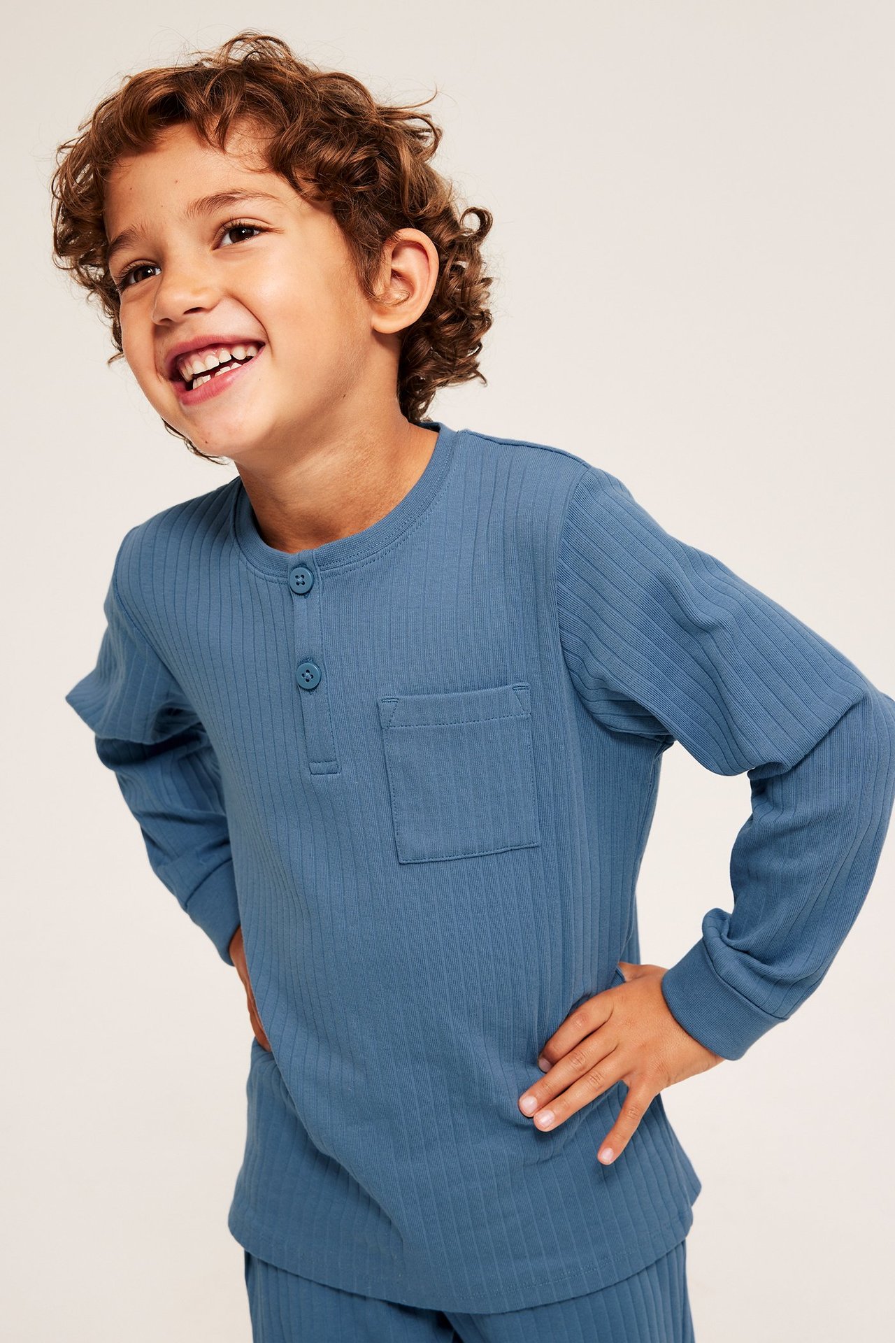 Etunäkymä: Lapsi sinisessä ribbipyjamassa; pitkähihainen yläosa napeilla ja rintataskulla.