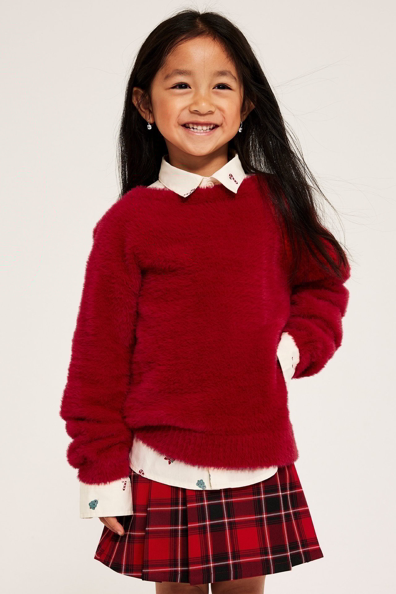 Tyttö punaisessa neulotussa villapaidassa, valkoinen paita ja raidallinen hame, etu.