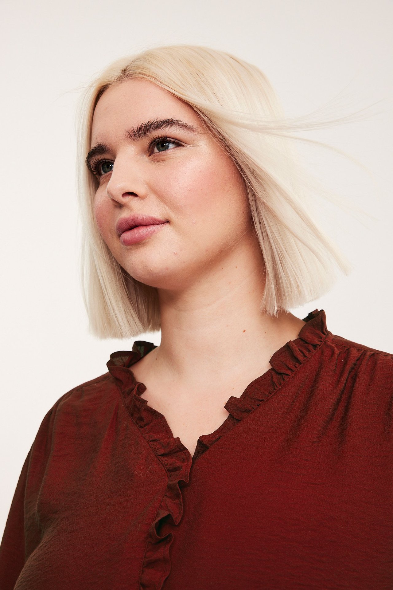 Närbild av en kvinna i en röd texturerad blus med volanger längs V-ringningen.