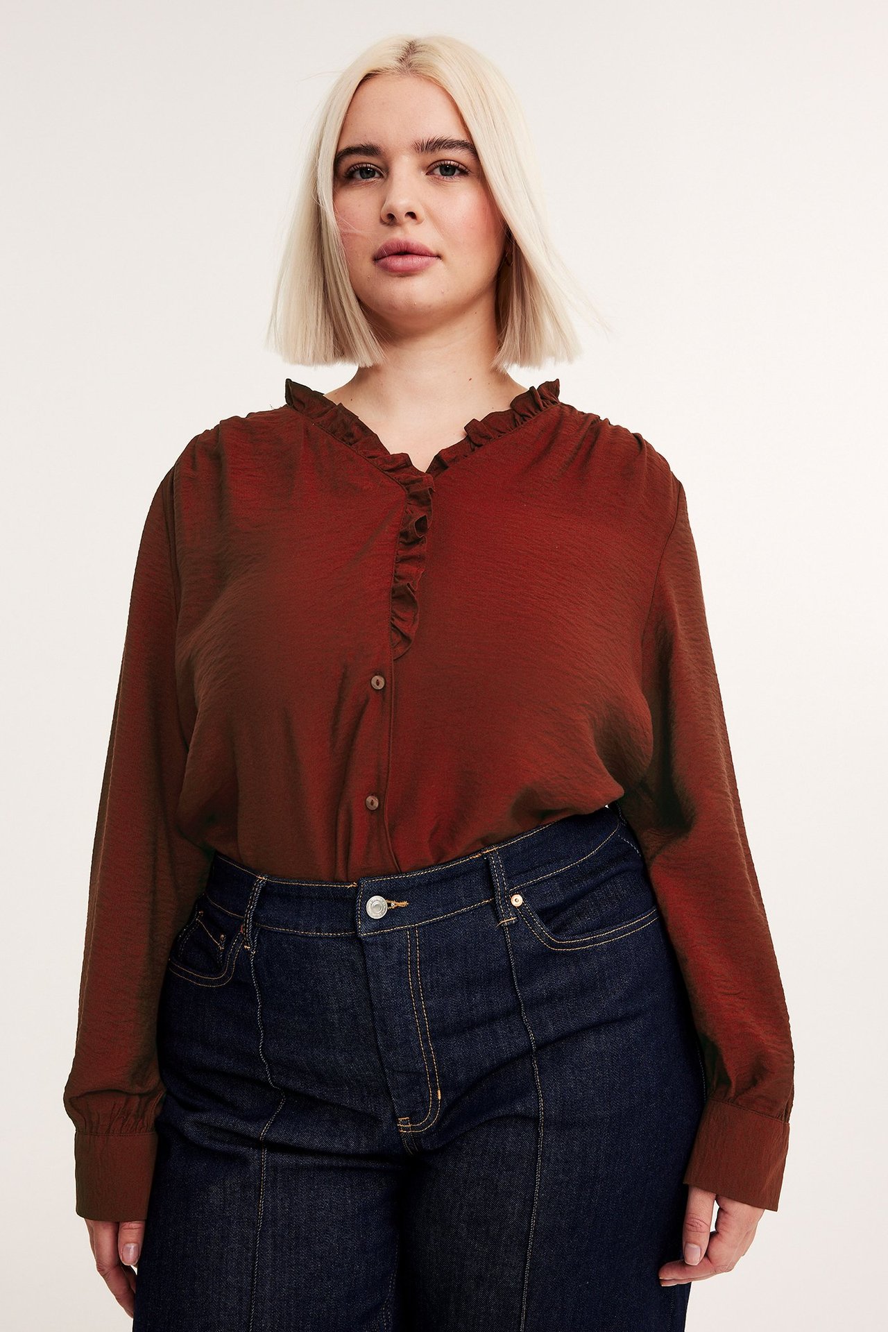 Framifrån: kvinna i röd volangblus med knappar och mörkblå jeans.