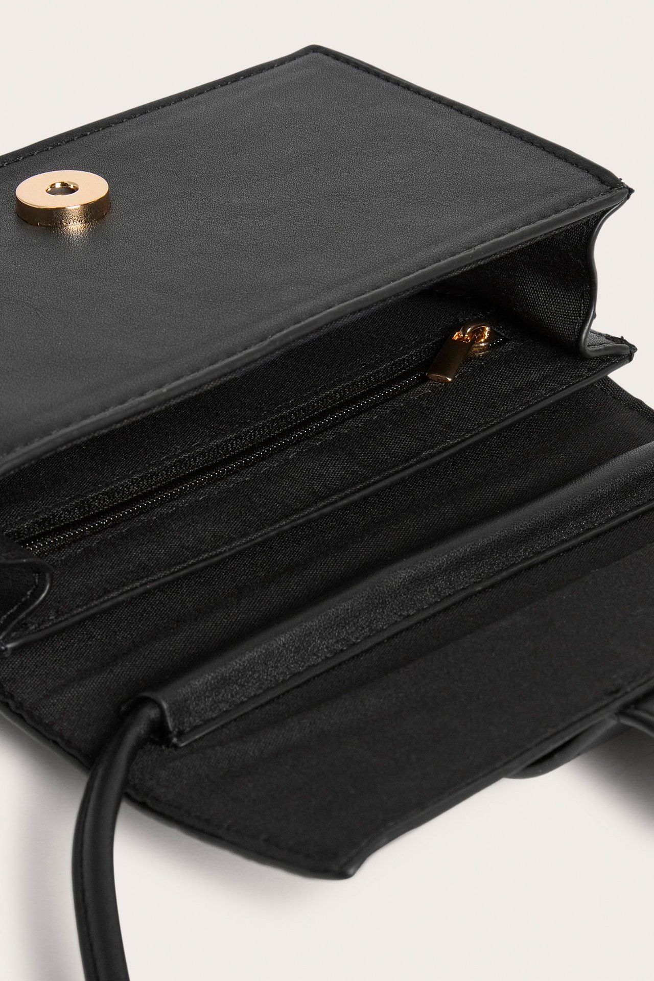 Zbliżenie z góry otwartej czarnej torebki na ramię ze sztucznej skóry, z magnetycznym zapięciem i wewnętrznym zamkiem.