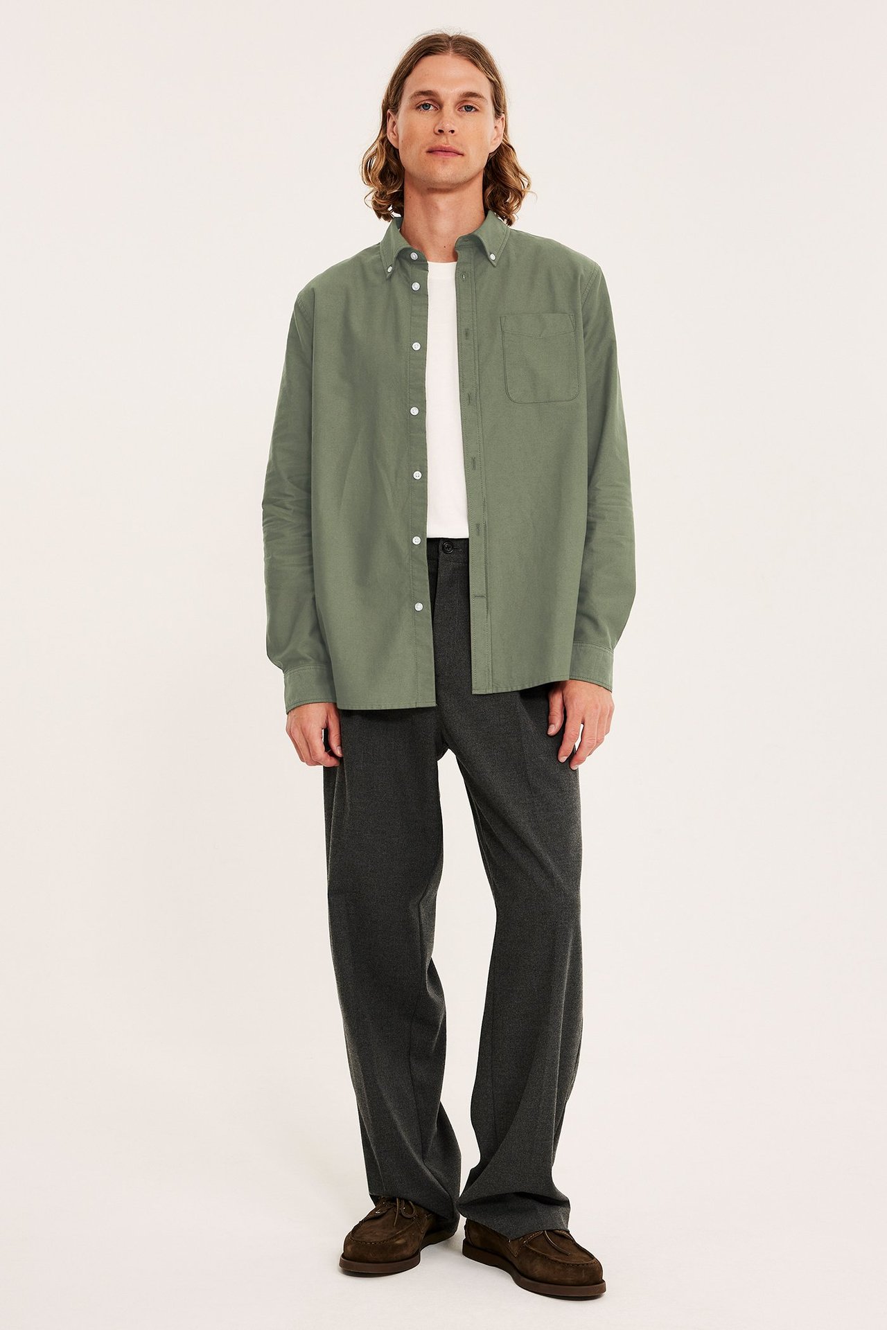 Edestä: mies vihreässä meleeratussa oxford-paidassa, valkoinen t-paita, tummanharmaat housut, ruskeat loaferit.